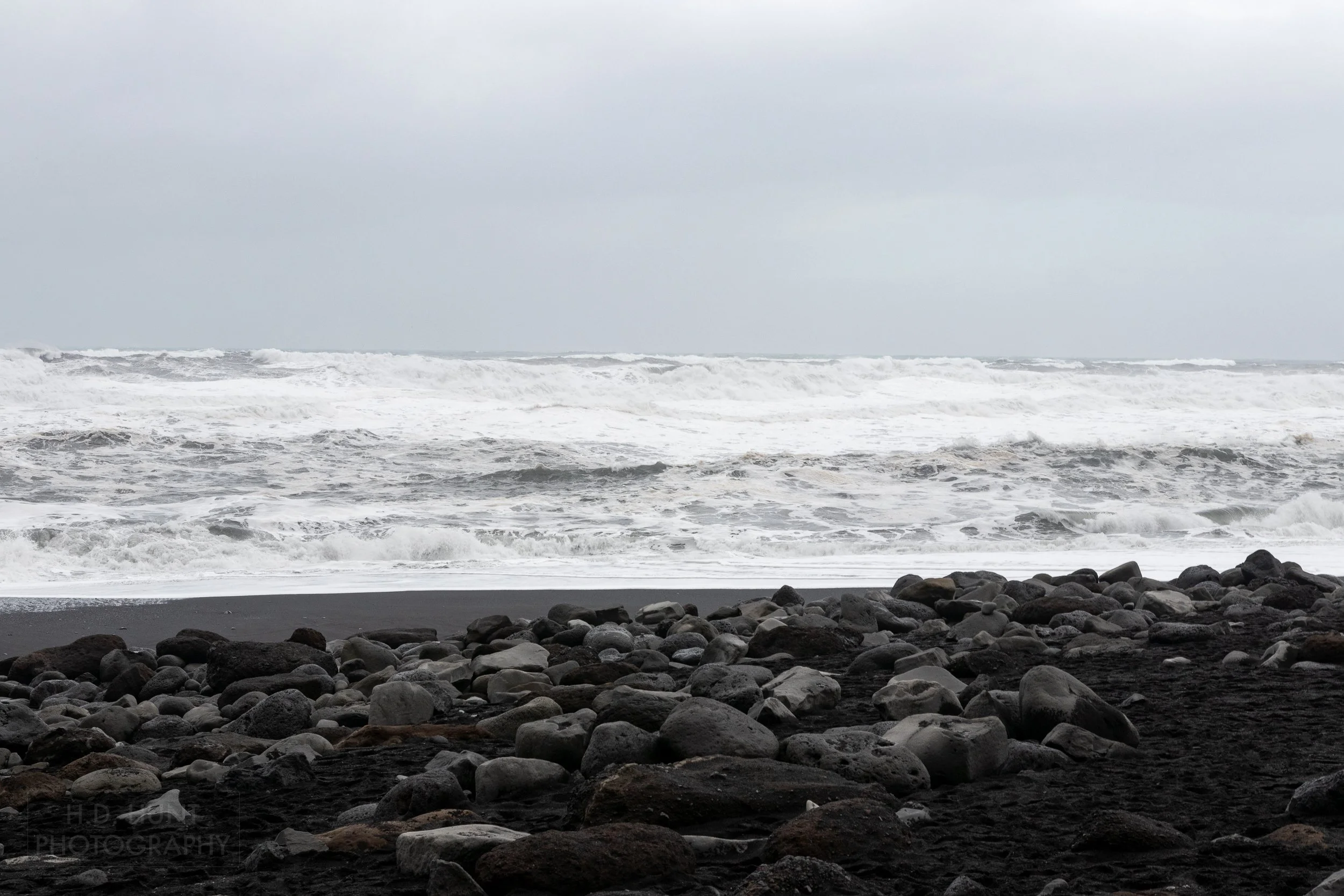 Tall whitecap waves crash against black sand and rock at Reynisfjara, Iceland
