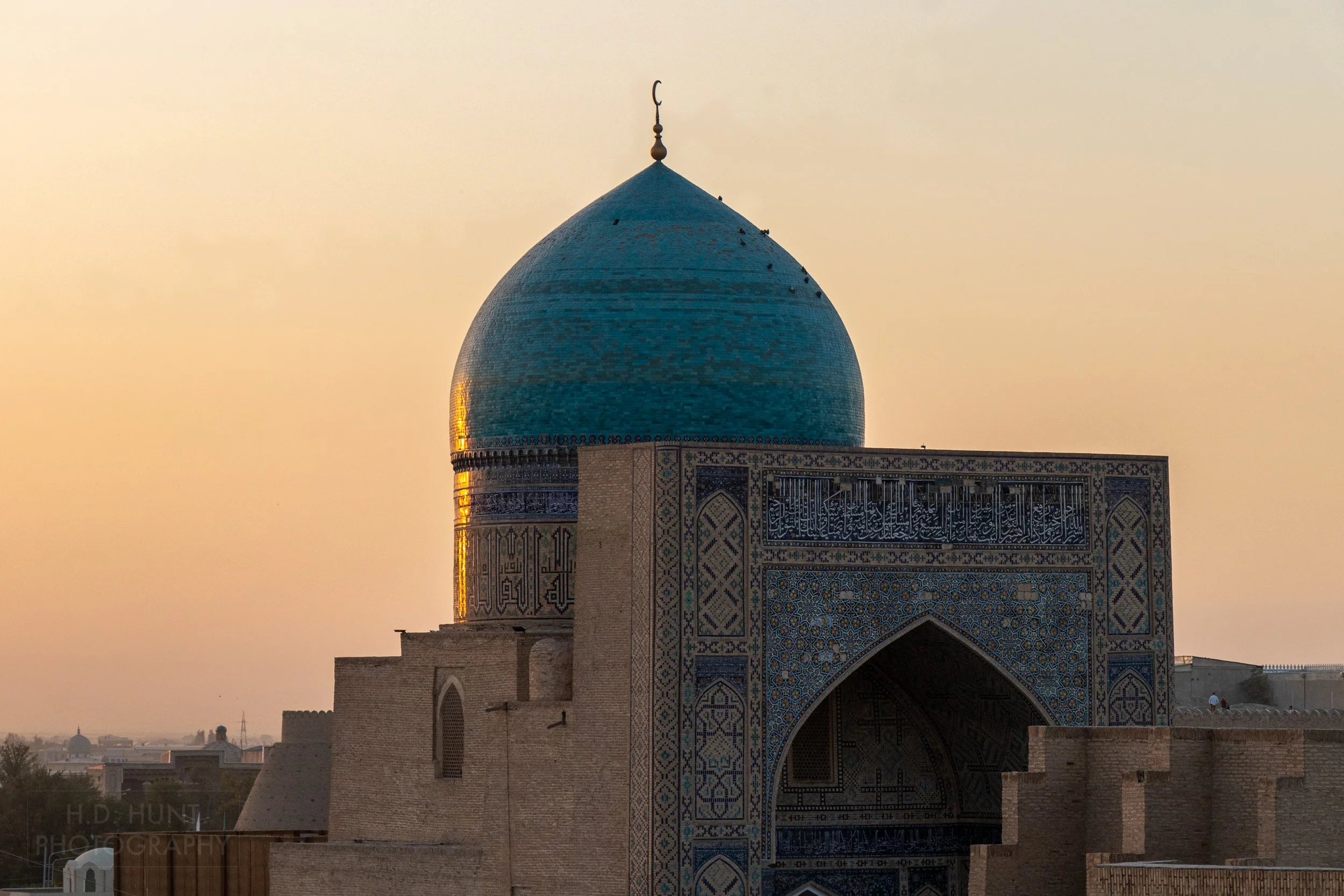 The sun sets behind the blue dome of the Kalan Mosque, Bukhara, Uzbekistan.
