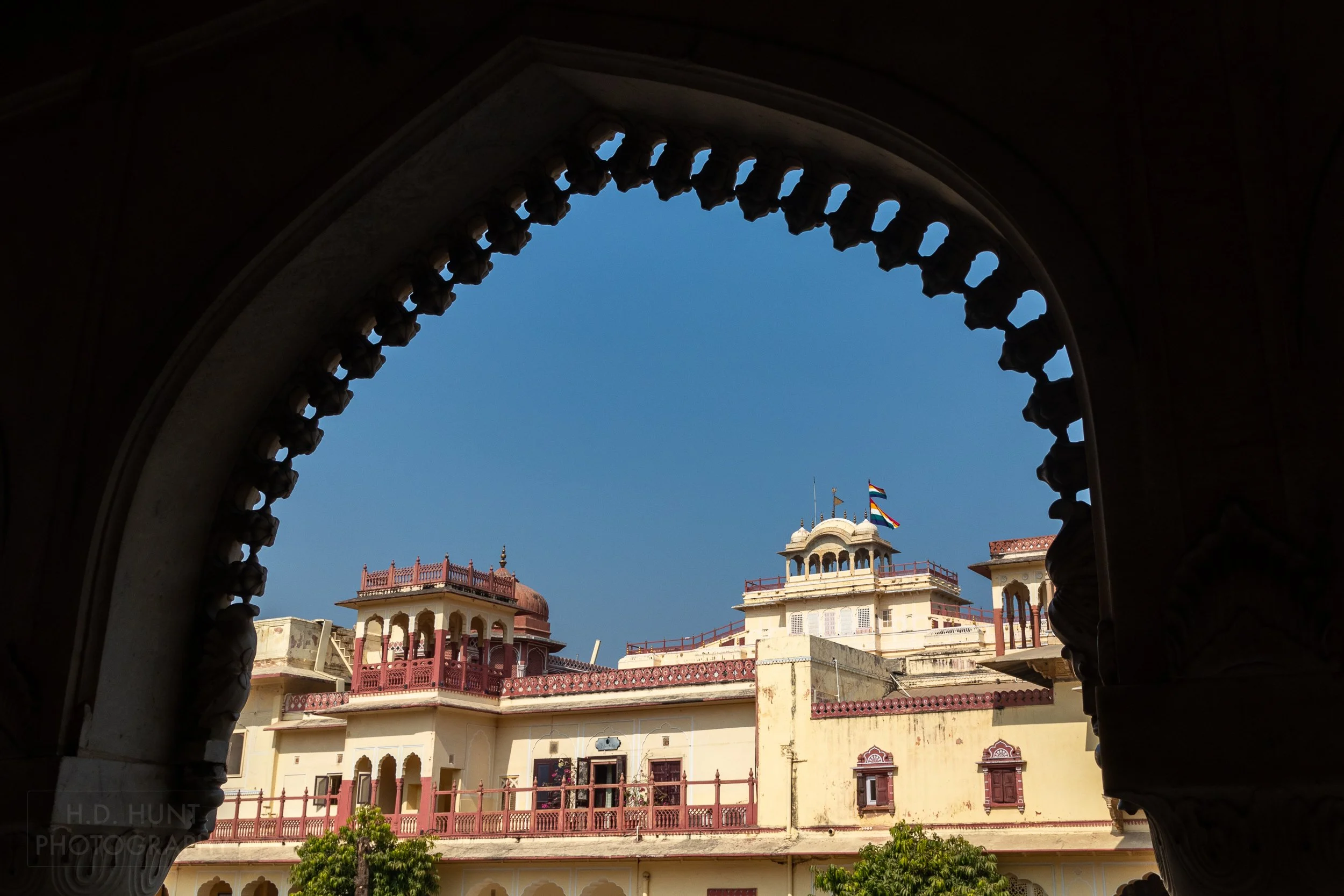 A large yellow and red stone building is seen through a rounded archway, City Palace, Jaipur, India.