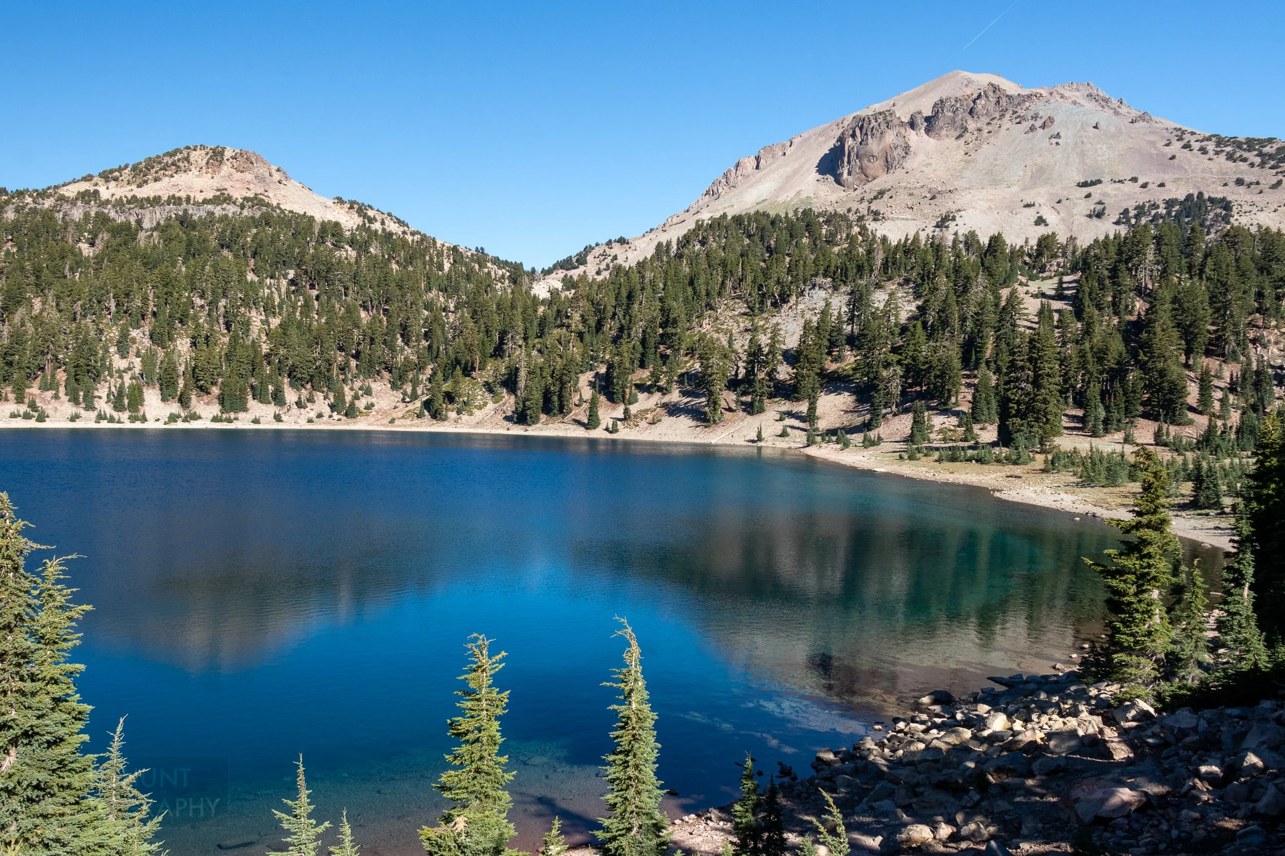 Two mountains rise behind a clear blue lake, Lassen Volcanic National Park, California, United States.
