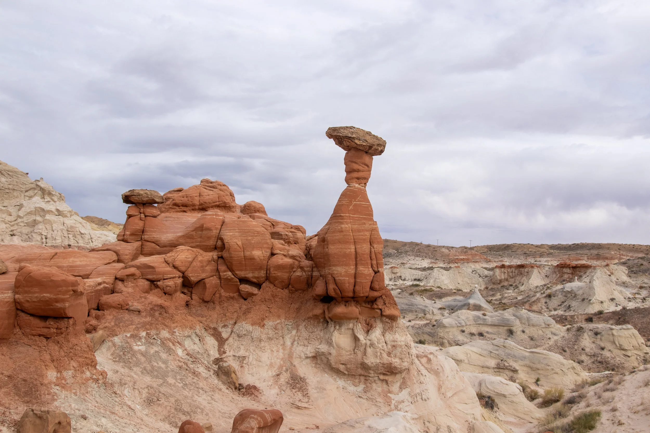 A large red sandstone column of rock with a flat boulder balanced on top of the column sits above a white rock valley, Toadstool Hoodoos, Grand Staircase - Escalante National Monument, Utah, United States.