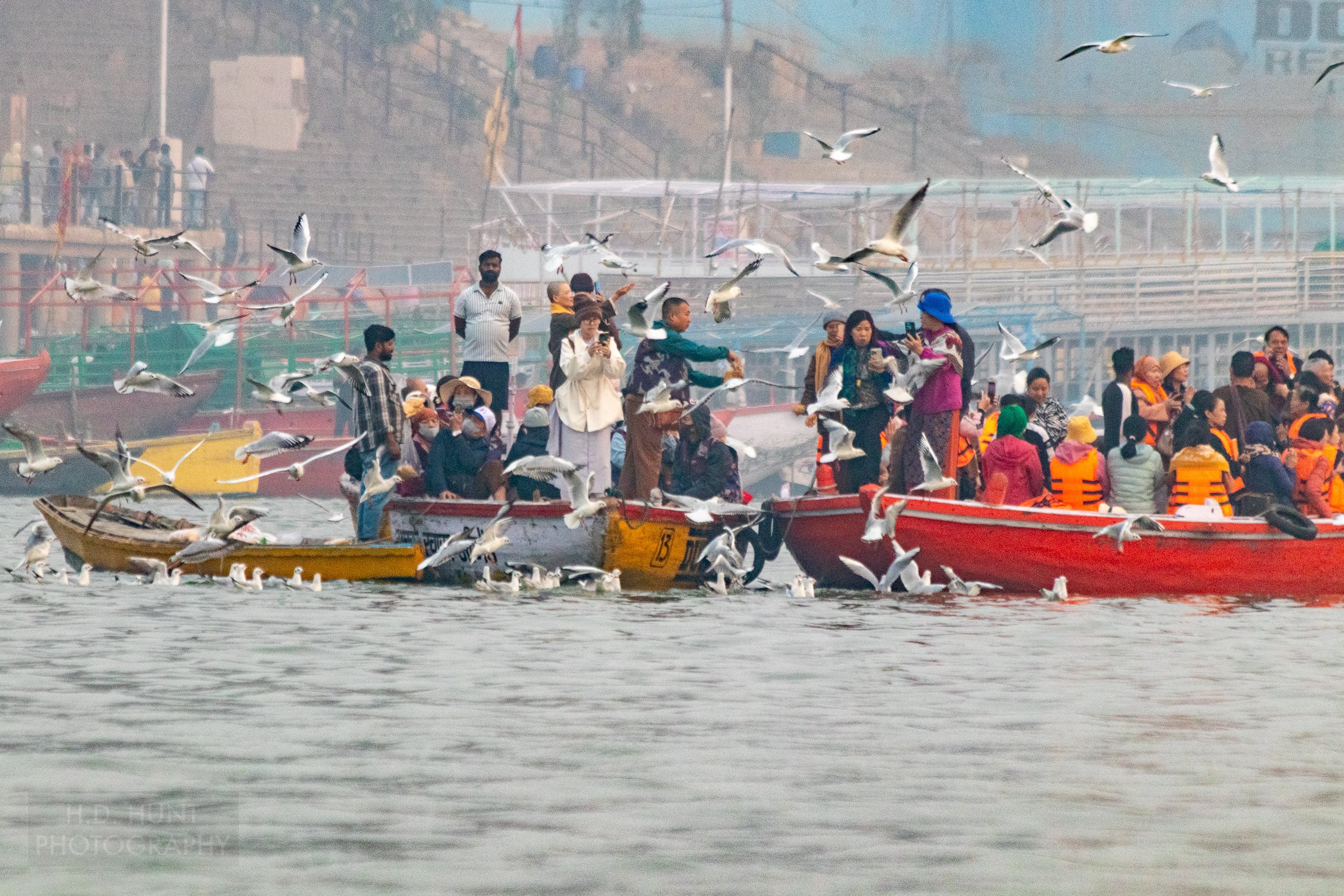 Tourists in boats on the Ganges River feed birds, Varanasi, India.
