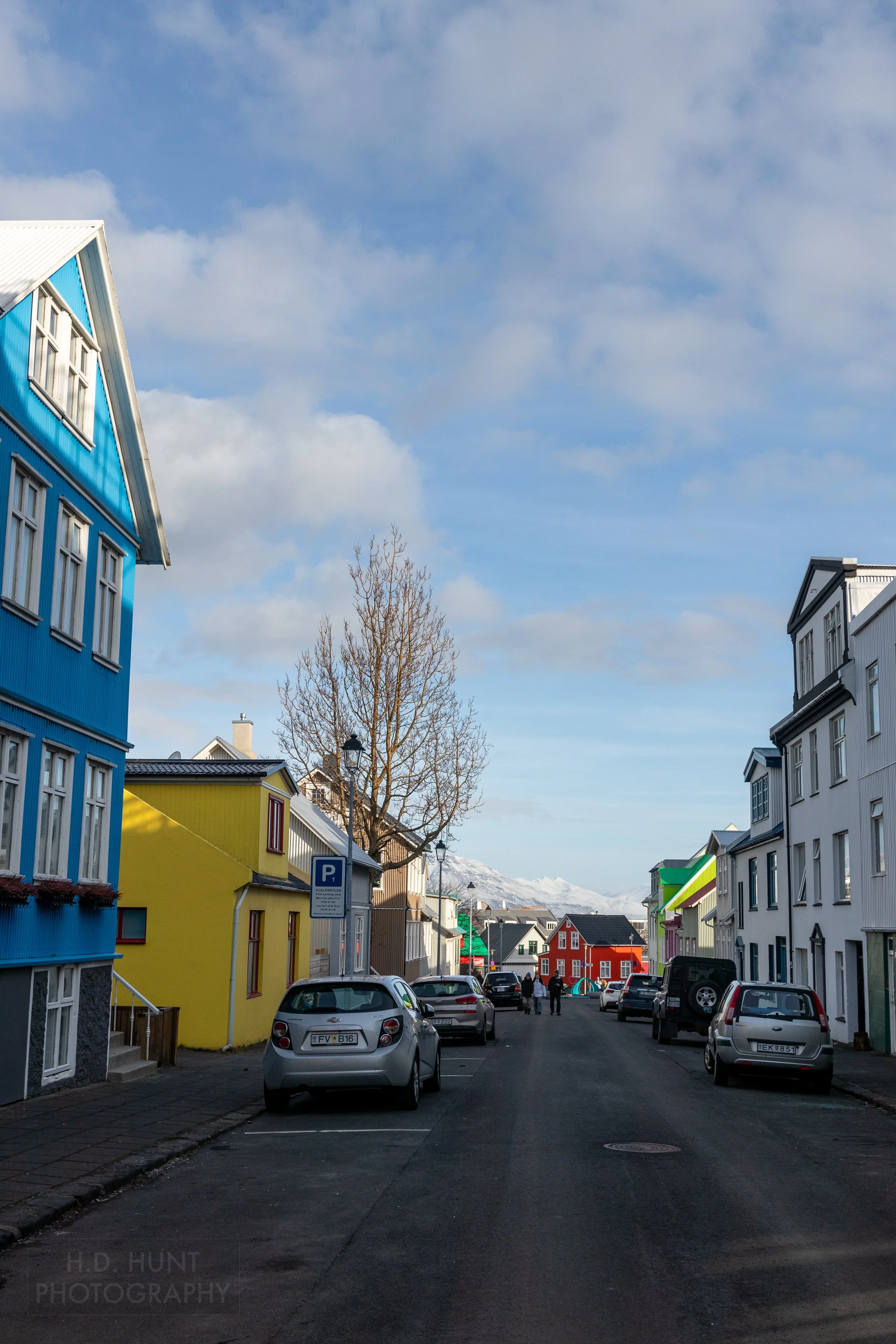 Several cars are parked along a street with several brightly colored houses on it, Reykjavík, Iceland.