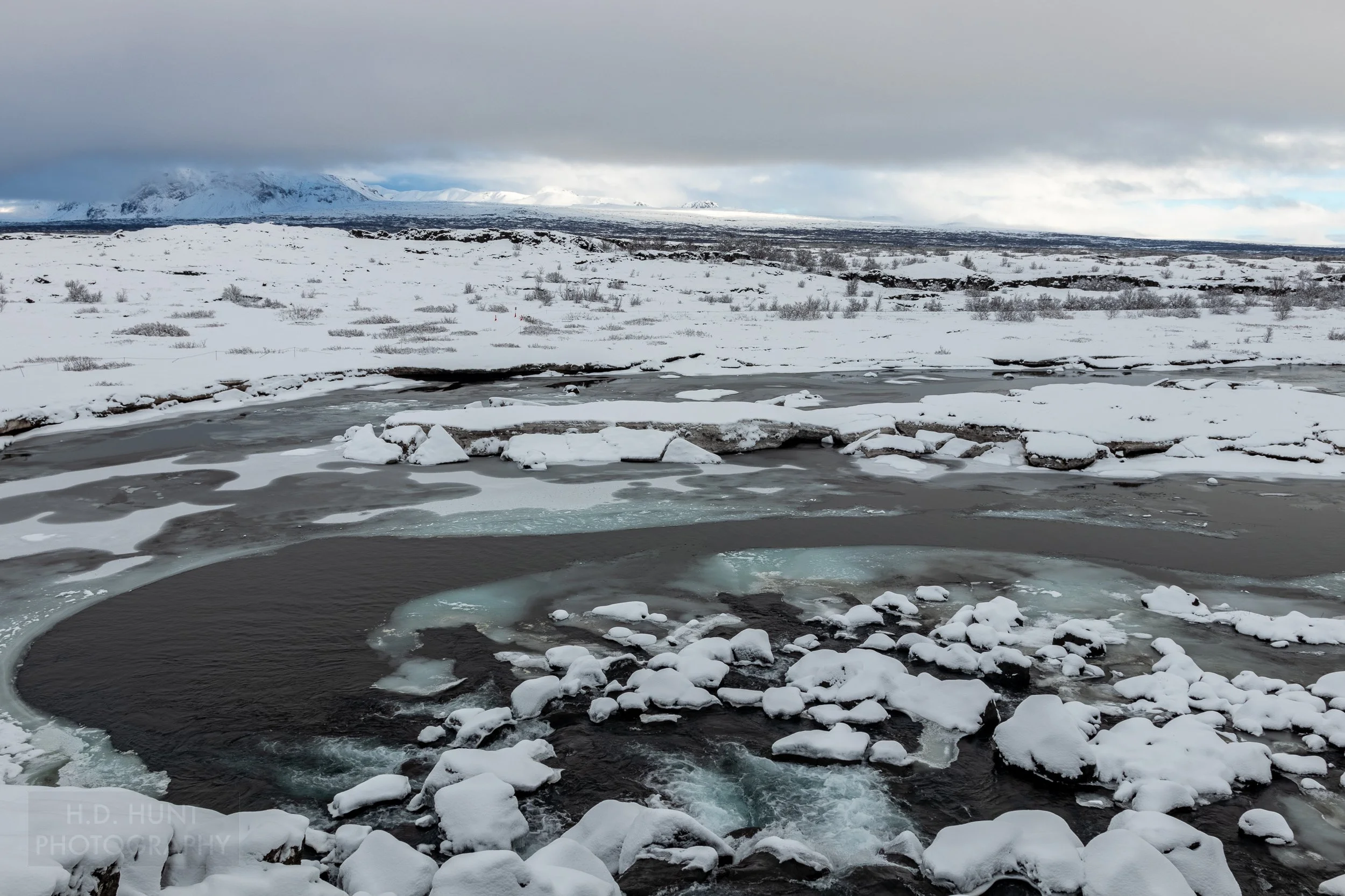 An icy river flows between small islands of snow-covered land, Þingvellir, Iceland.