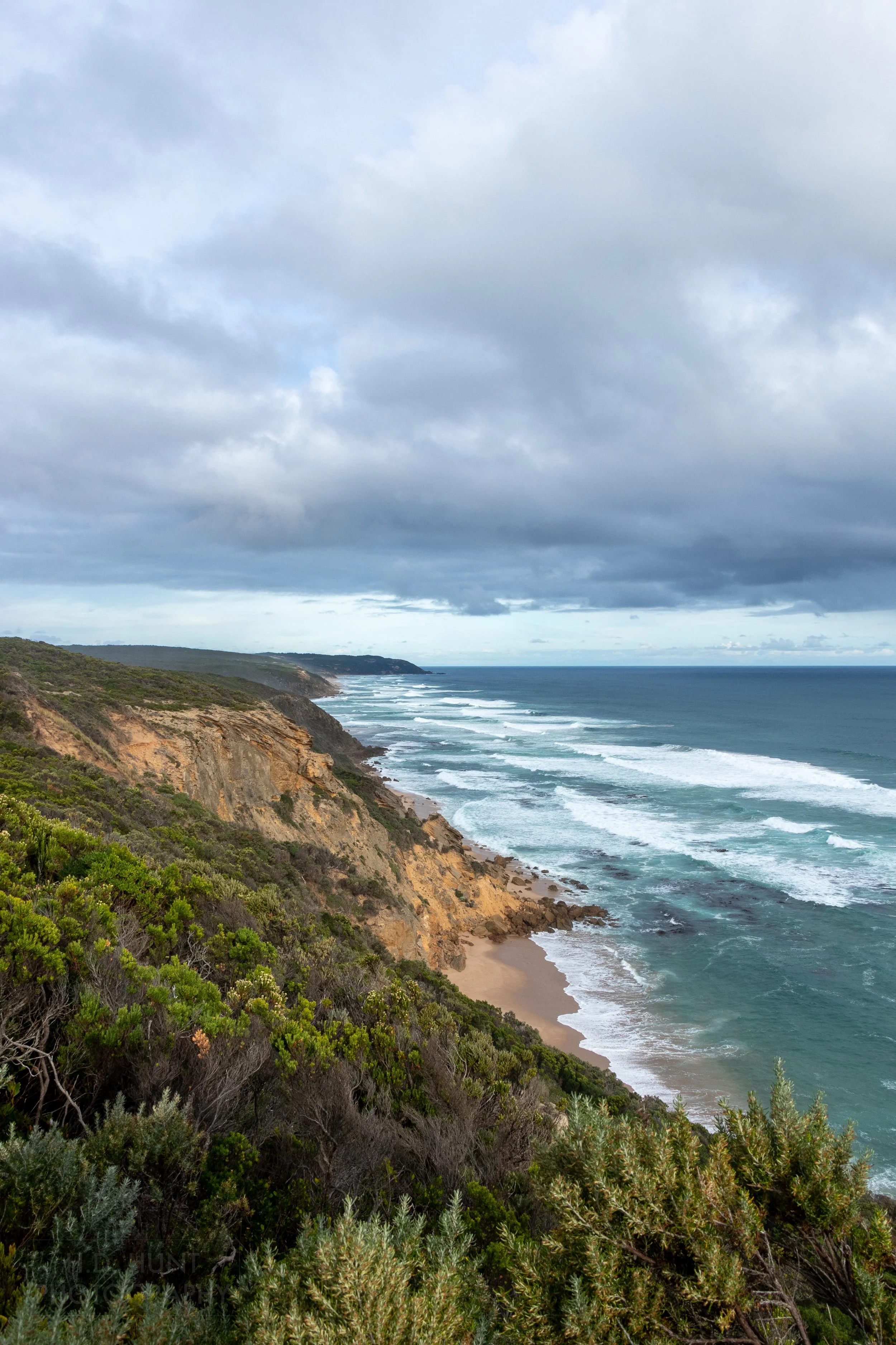 The white waves of the blue Southern Ocean crash against tall brown cliffs along The Great Ocean Walk, Victoria, Australia.