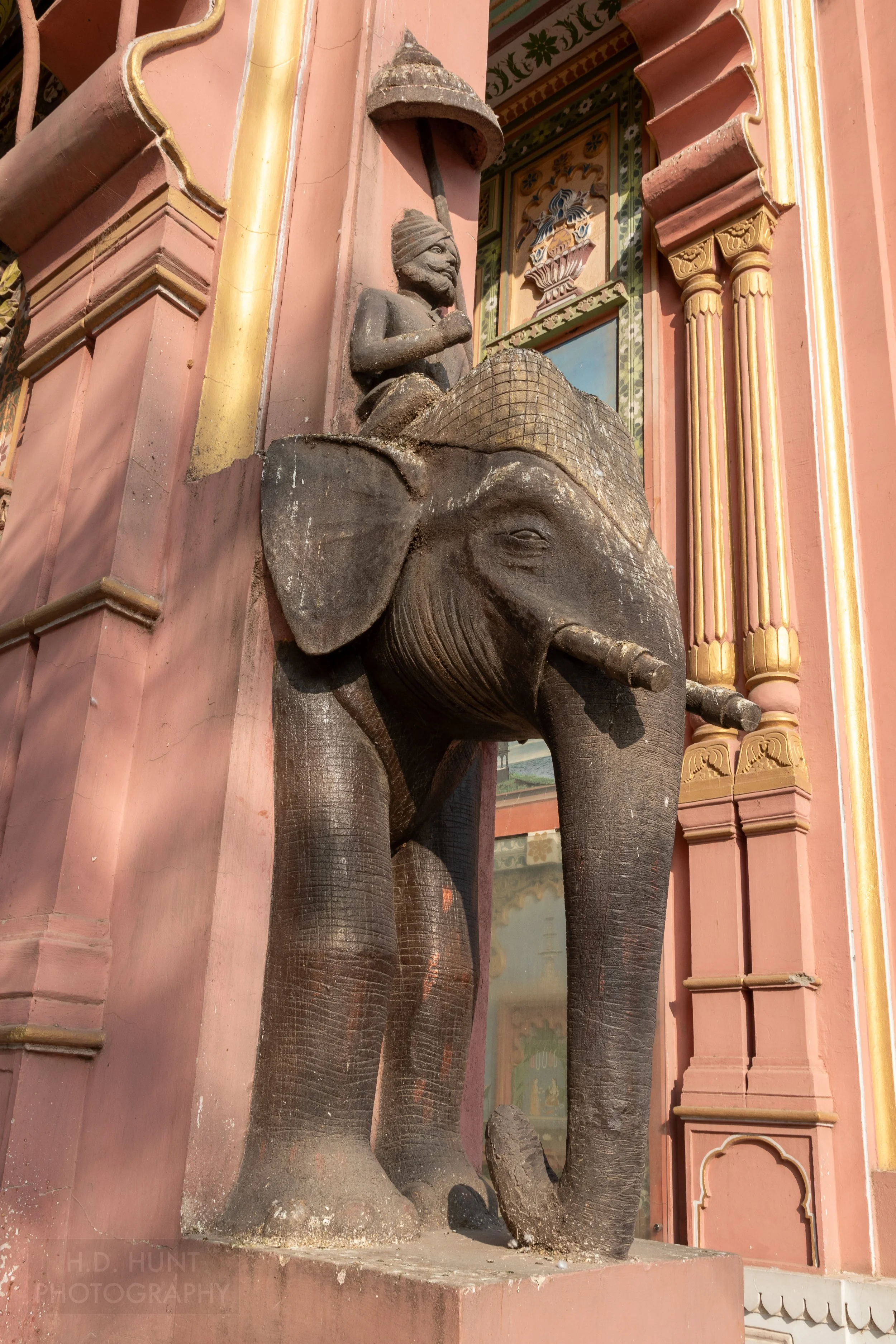 A dark stone elephant figure is attached to a pink-colored column, Patrika Gate, Jaipur, India.