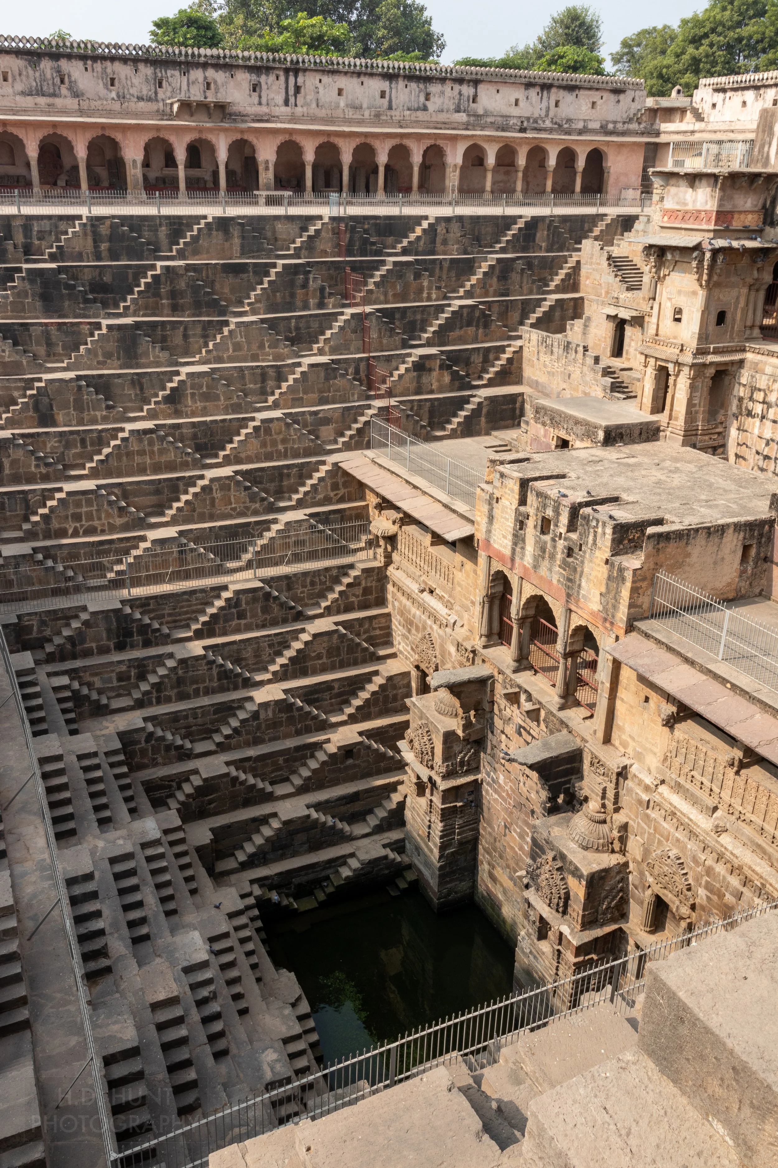 The zig-zag tan stone steps of Chand Baori rise from a small water well in the ground, Abhaneri, India.