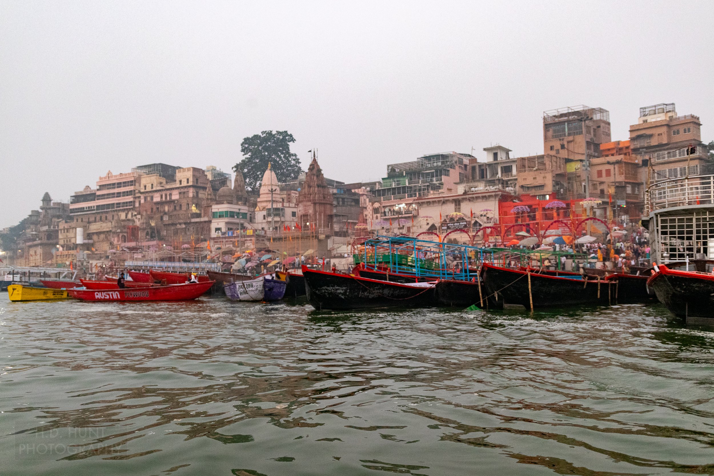 Multiple tied-up boats in the Ganges River rest in front of several temple buildings along the river's edge, Varanasi, India.
