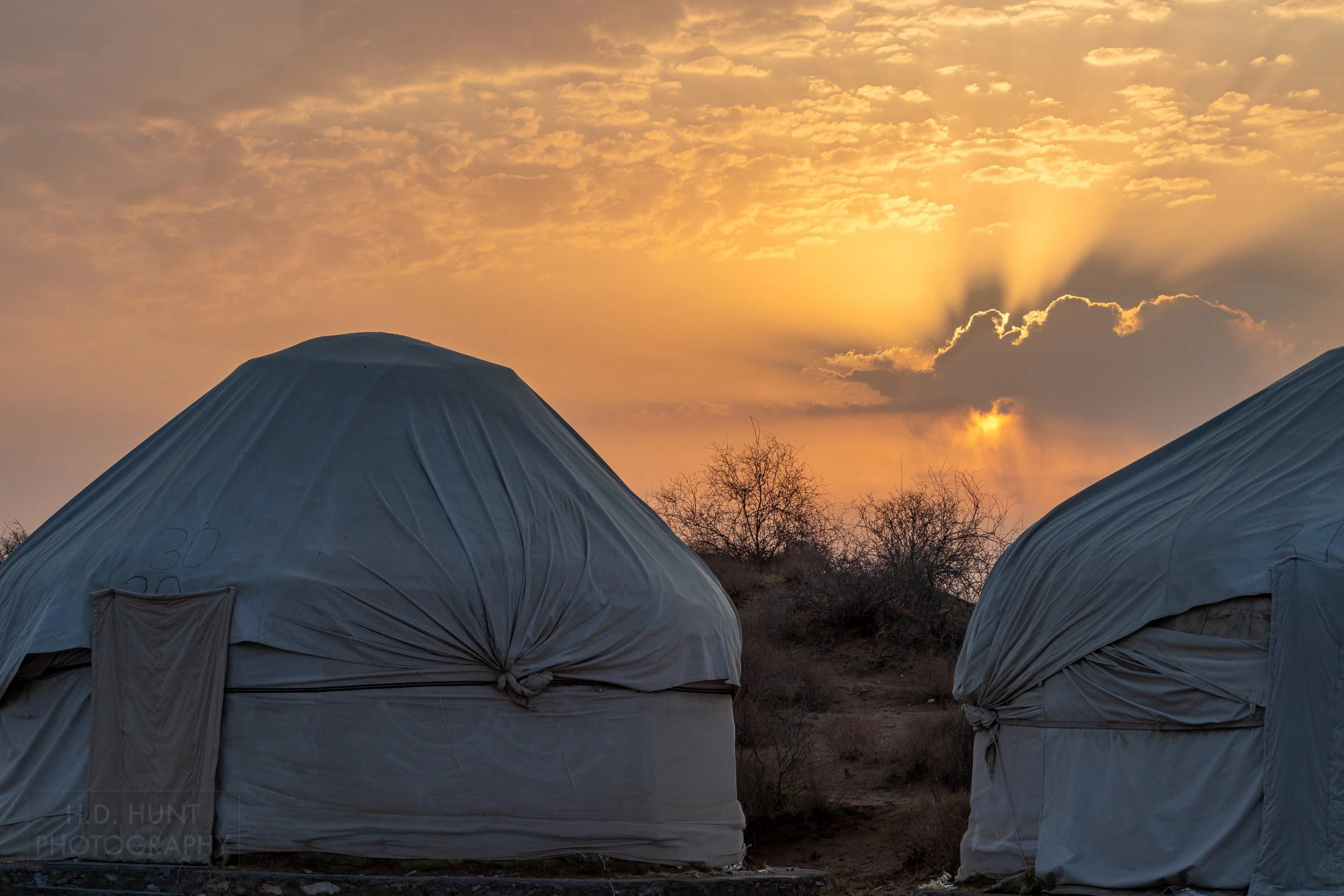 The sunrise peaks out from the clouds behind two yurts, Yangikazgan, Uzbekistan.