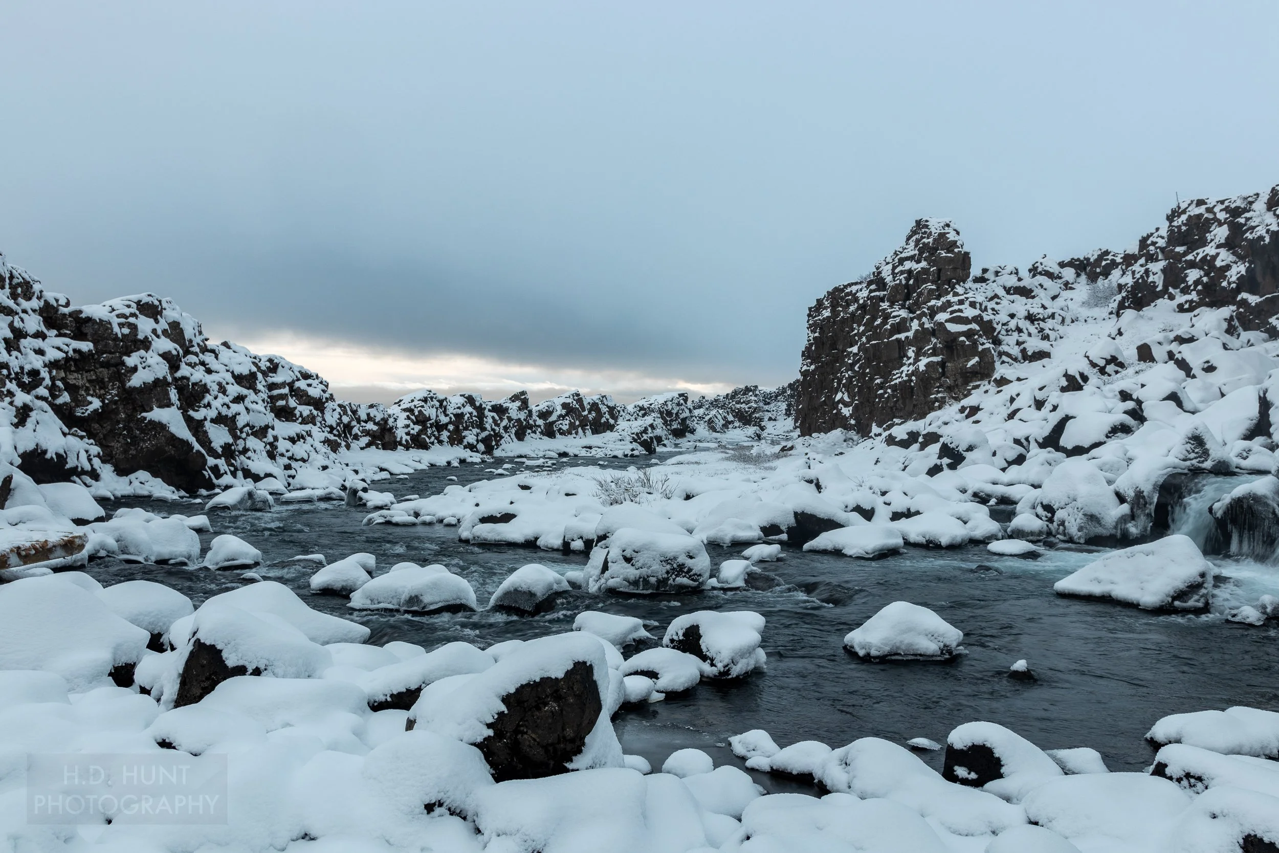 A river runs between two rocky cliff faces at Þingvellir, Iceland.