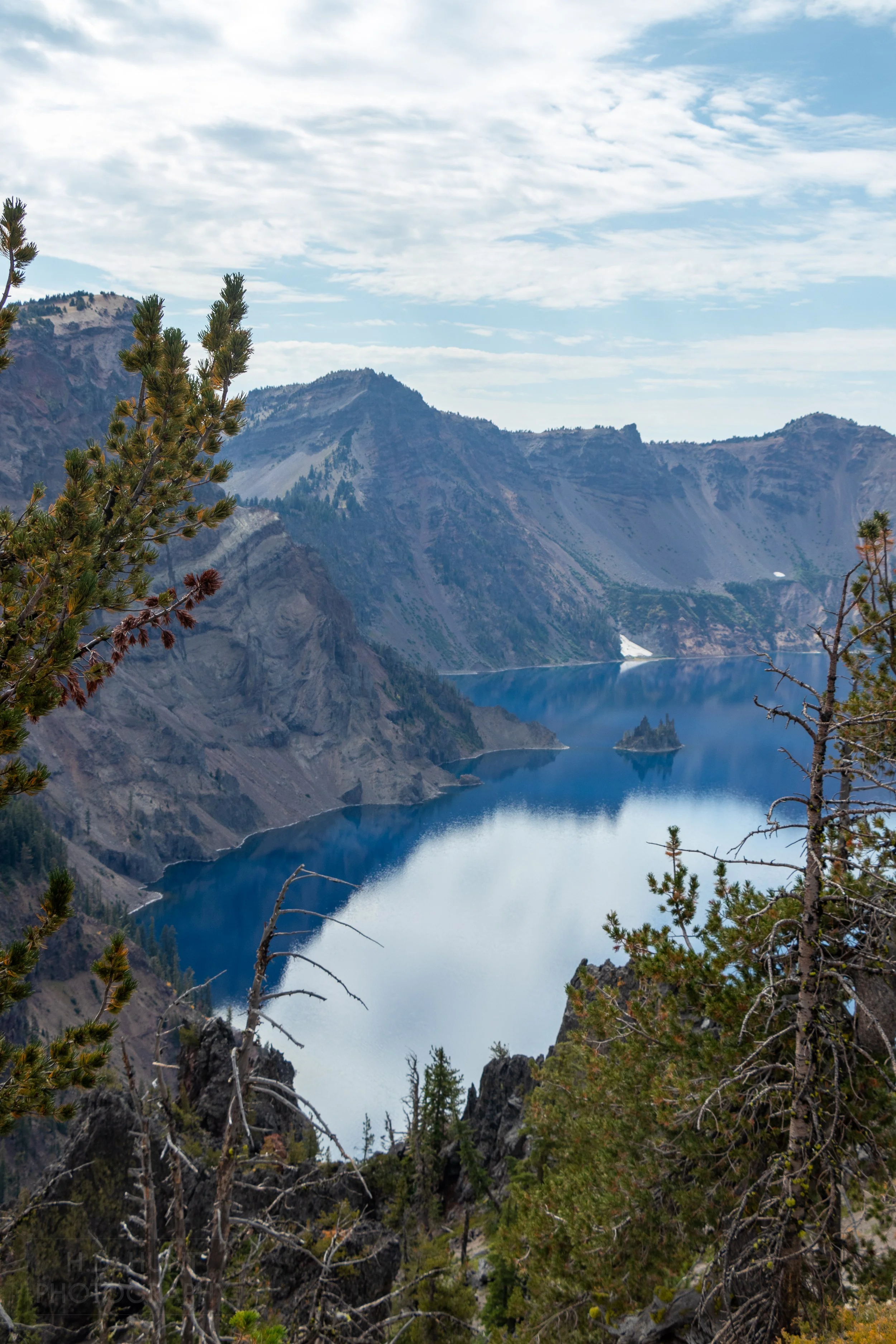 The deep blue waters of Crater Lake surrounded by the high cliffs of the Mount Mazama caldera, with the Phantom Ship reaching out above the waterline, Crater Lake National Park, Oregon, United States.