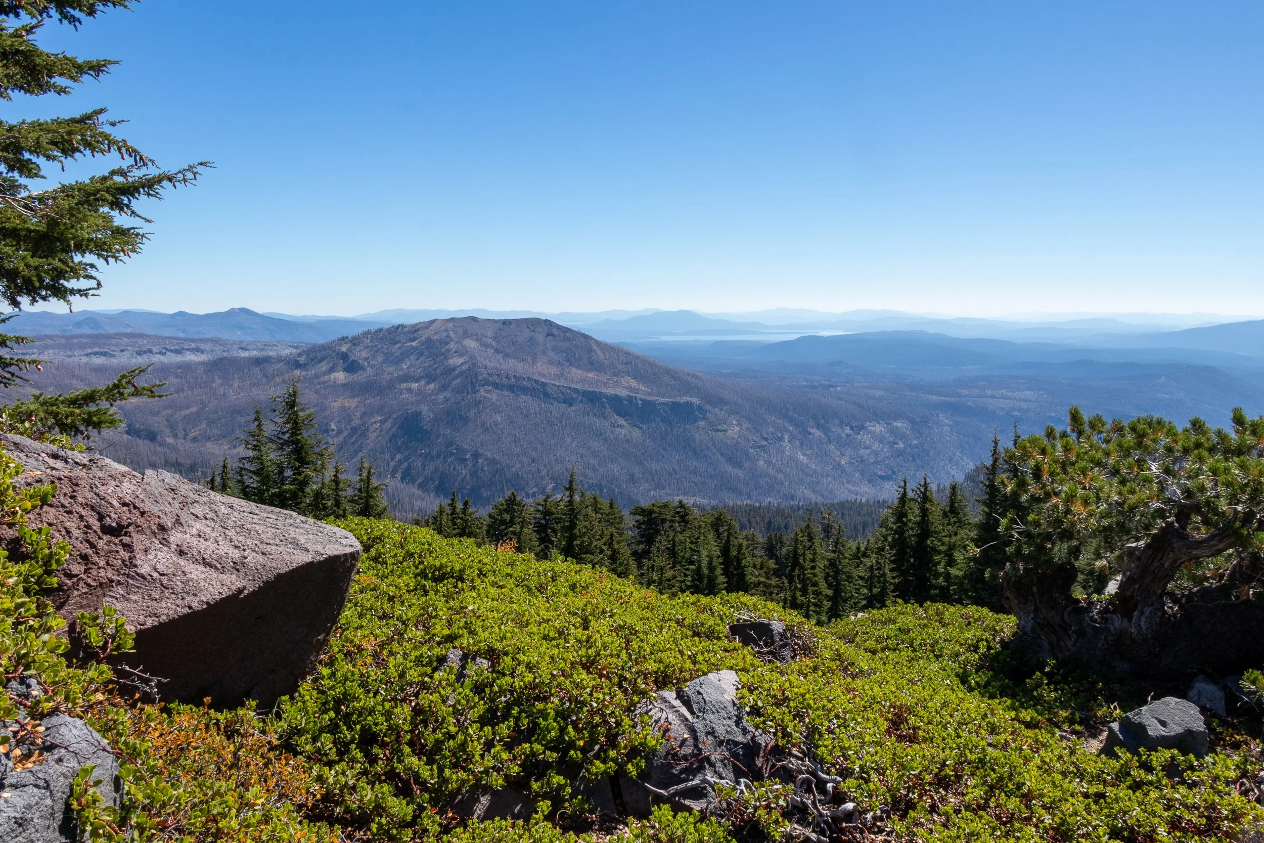 A green meadow in the foreground gives way to a view of a small mountain in the mid-ground and a lake far in the distance, Lassen Volcanic National Park, California, United States.