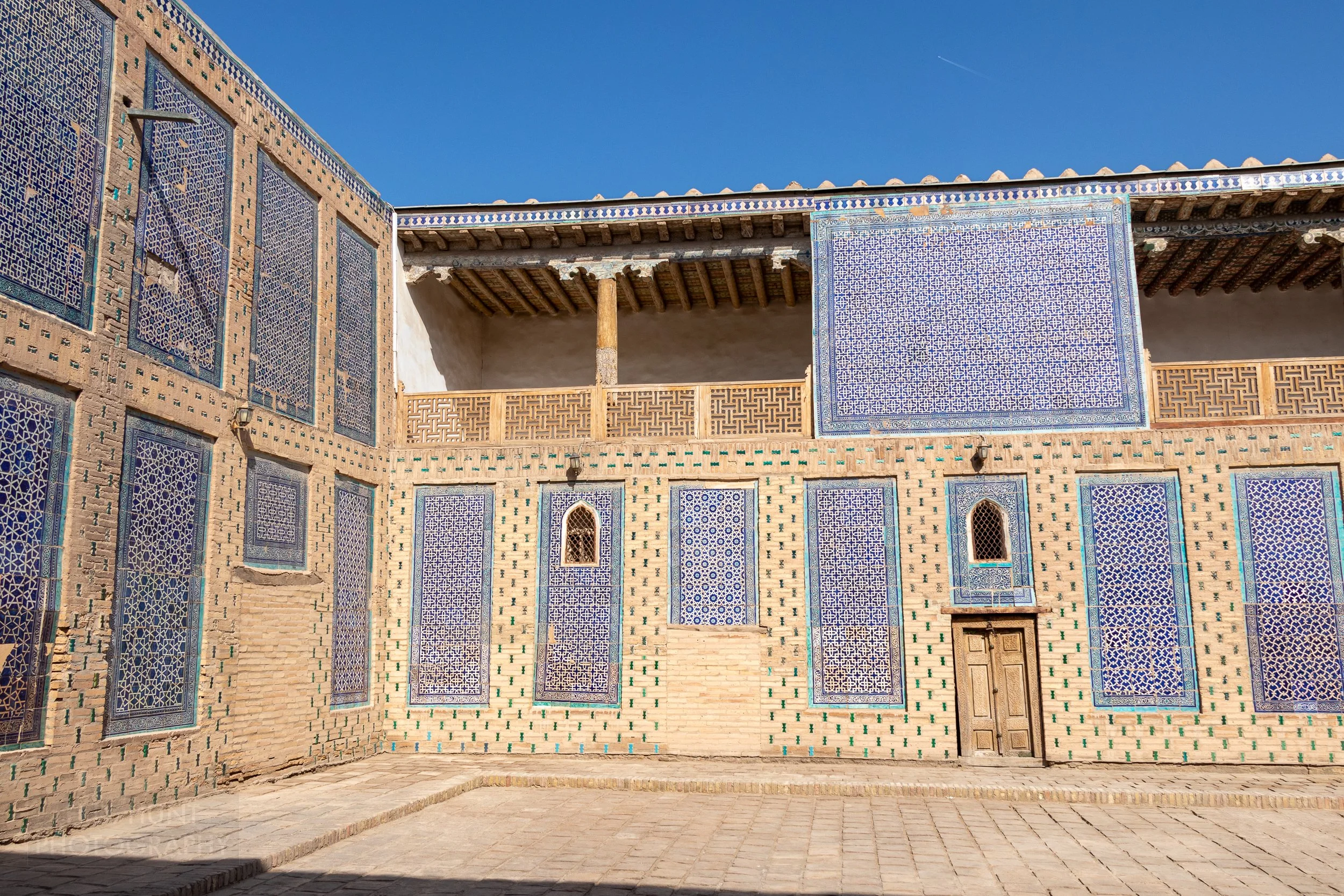 A tan stone-walled courtyard featuring blue and white tiled rectangles at Toshhovli Palace, Khiva, Uzbekistan.