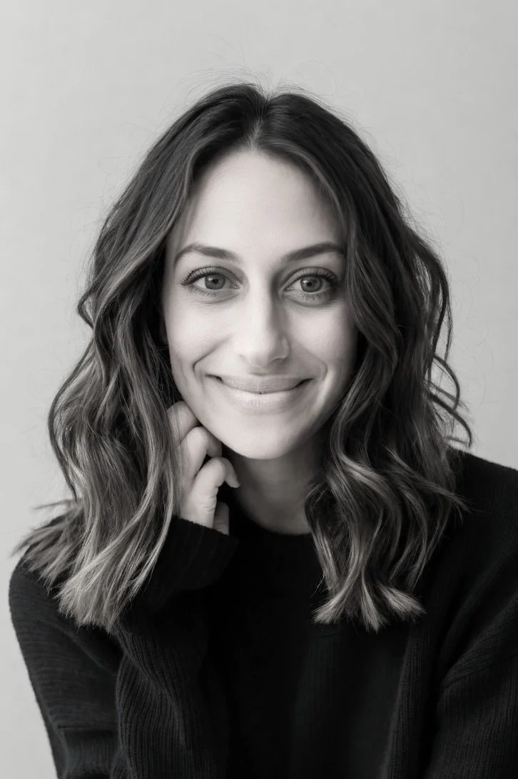 Black and white portrait of a smiling woman with wavy hair wearing a dark sweater, looking at the camera.