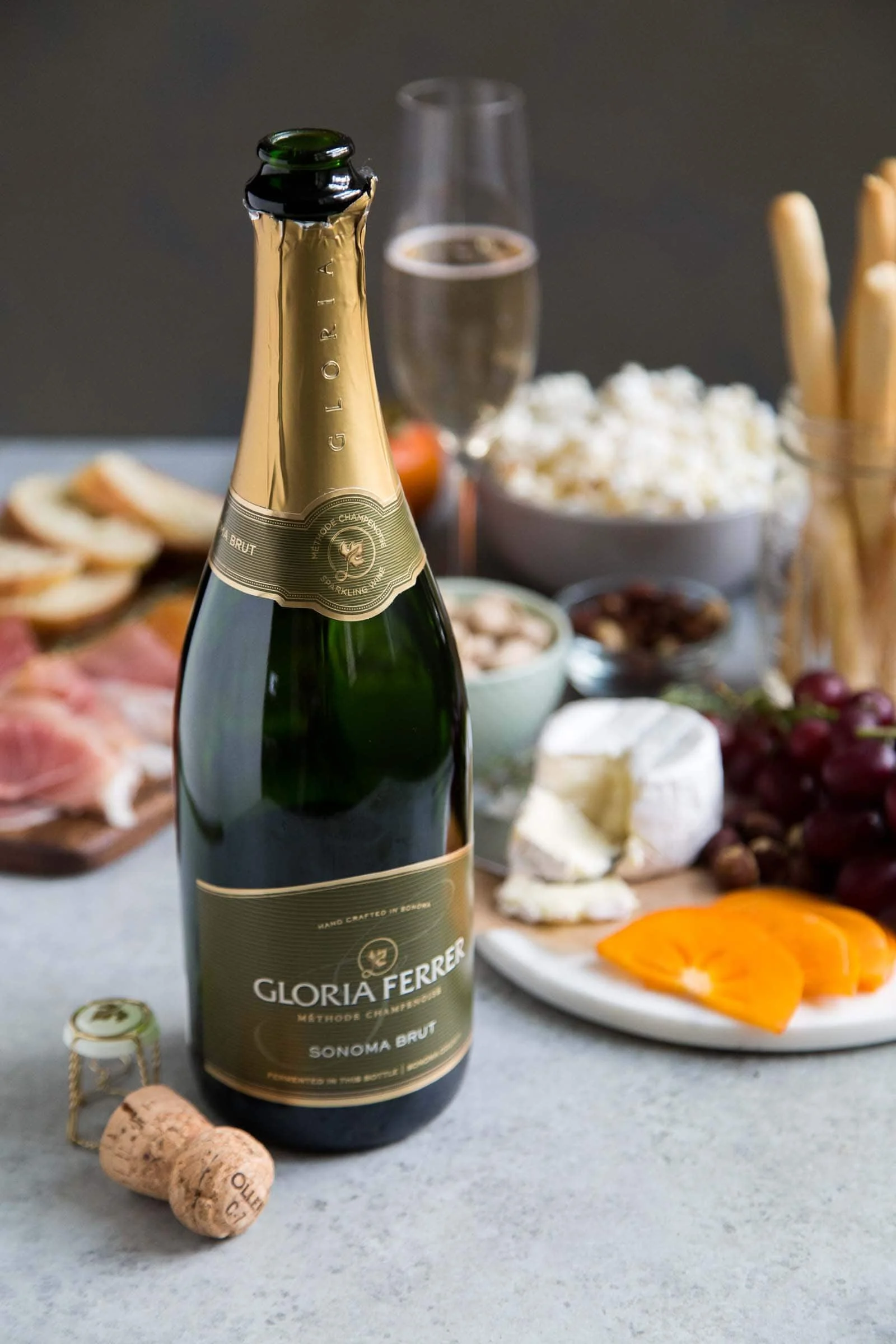 Bottle of Gloria Ferrer Sonoma Brut with a spread of salty snacks to enjoy.