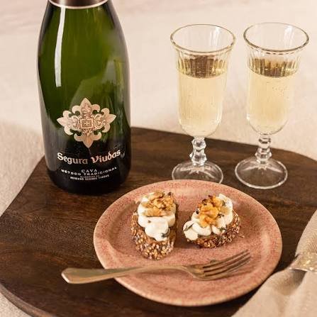 Bottle of Segura Viudas Cava with two vintage glasses and goat cheese crostini with candied walnuts.