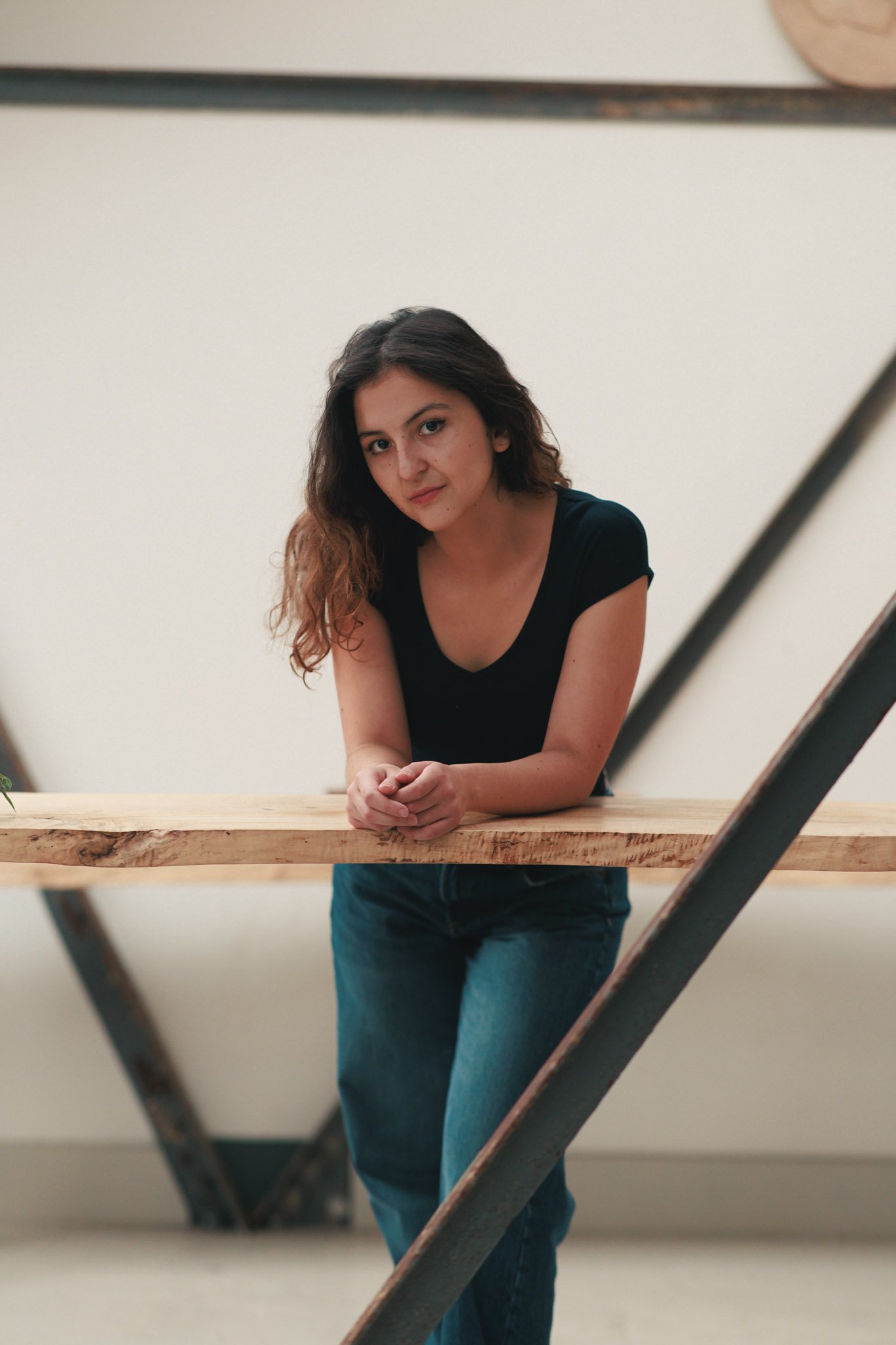 A young woman leaning on a wooden table, looking at the camera with a slight smile.