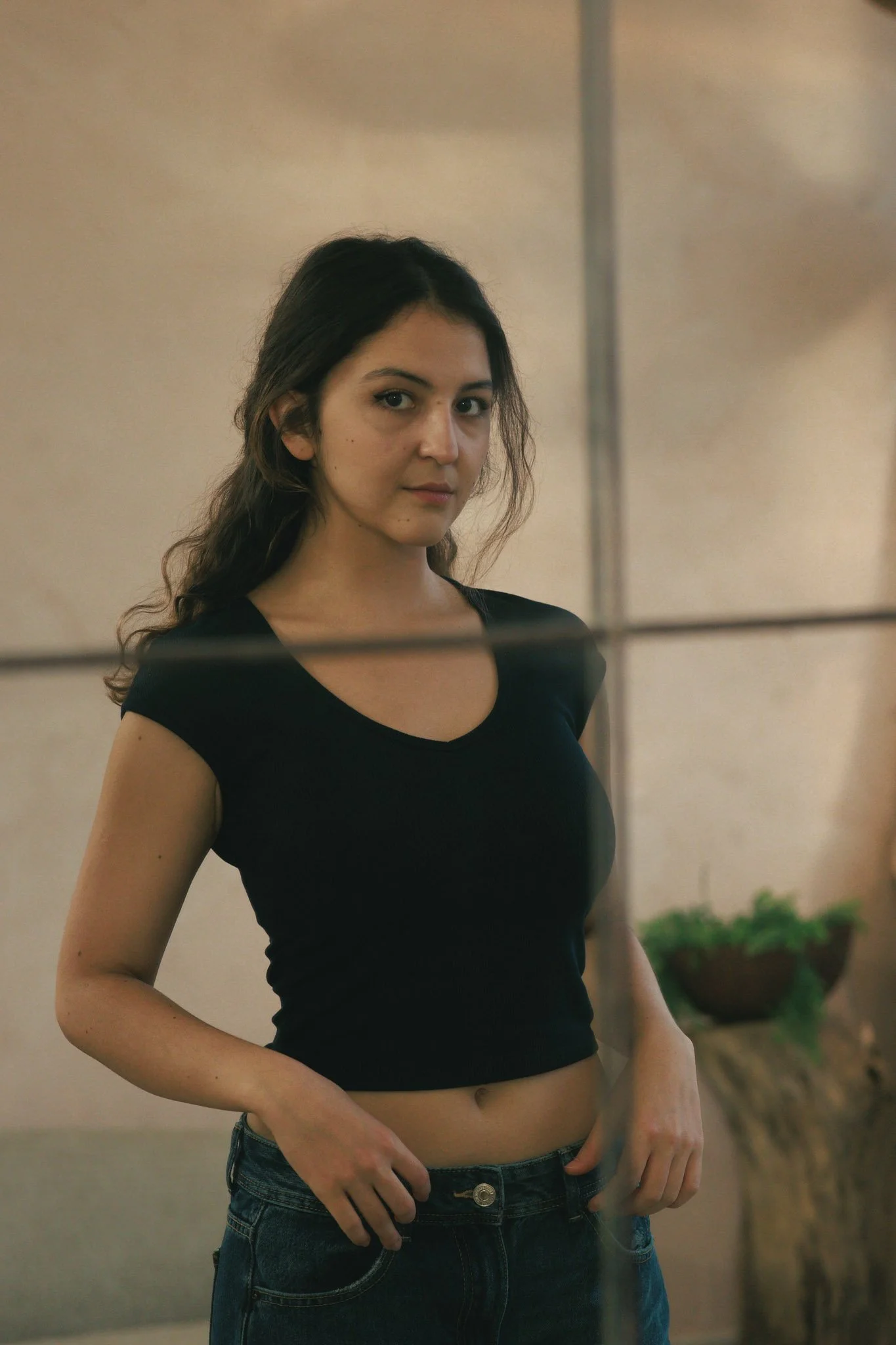 A young woman with dark hair and a black t-shirt looking at the camera through a glass wall.