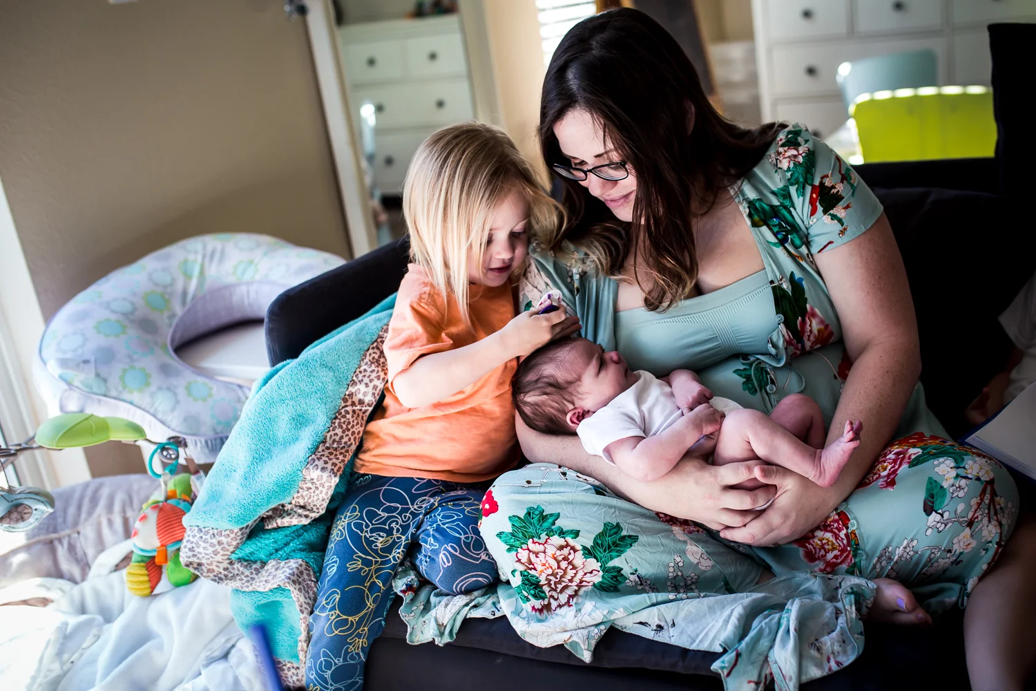 A mother and new big sister cuddle and smile at their newborn baby during a documentary newborn session in Clermont, Florida.