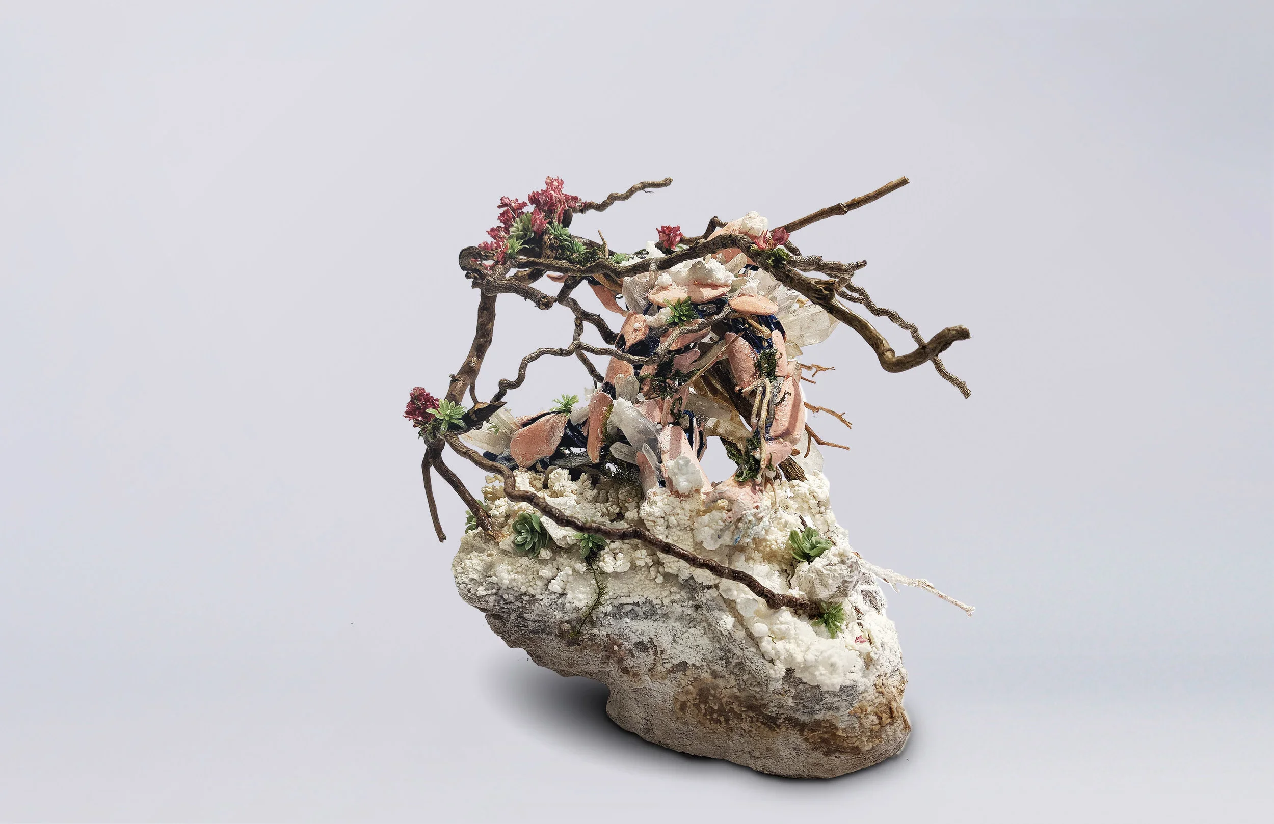A miniature sculpture of a animal constructed with twigs, small plants, rocks, and other natural materials on a piece of white porous material.