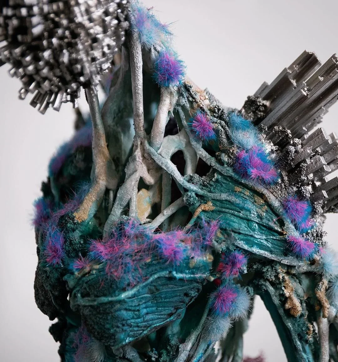 Close-up of an abstract sculpture featuring metallic textures, colorful fluffy fibers in purple, pink, and blue, and spiky metallic elements.