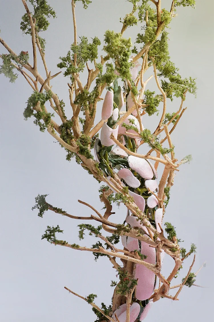 A tree with sparse branches and green moss, intertwined with a pink and green robotic arm or mechanical structure.
