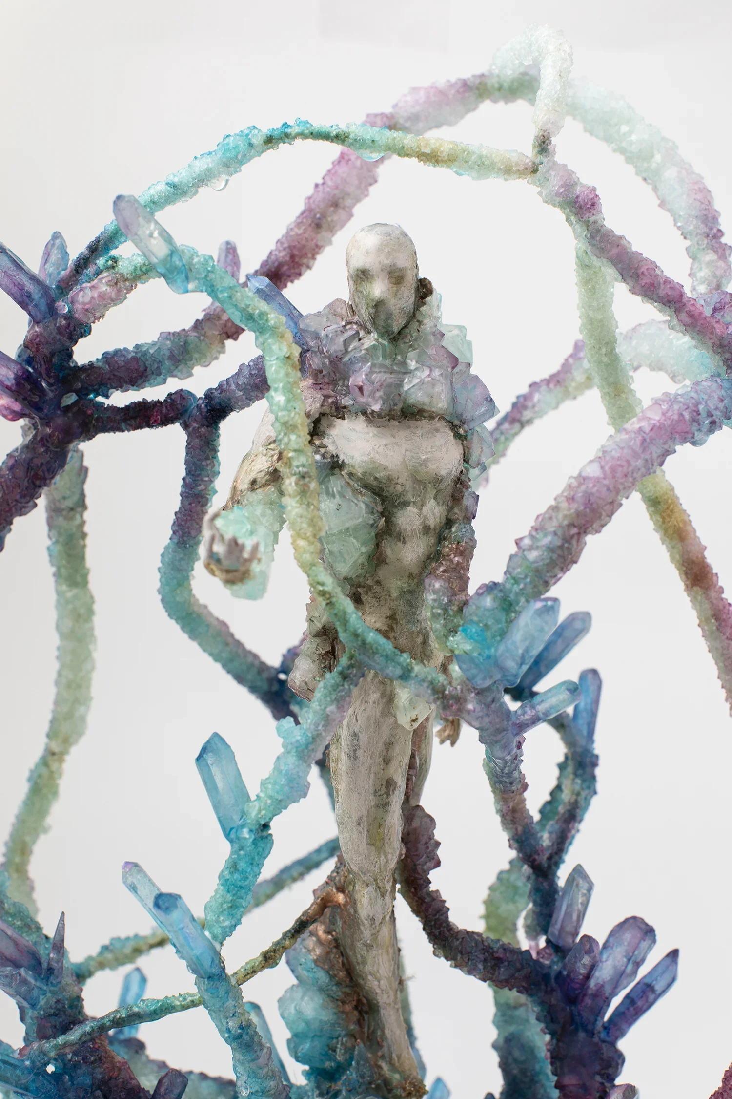 Mixed media sculpture combining a human-like face with intertwined rainbow-colored cables or wires, and decorated with crystal-like formations.