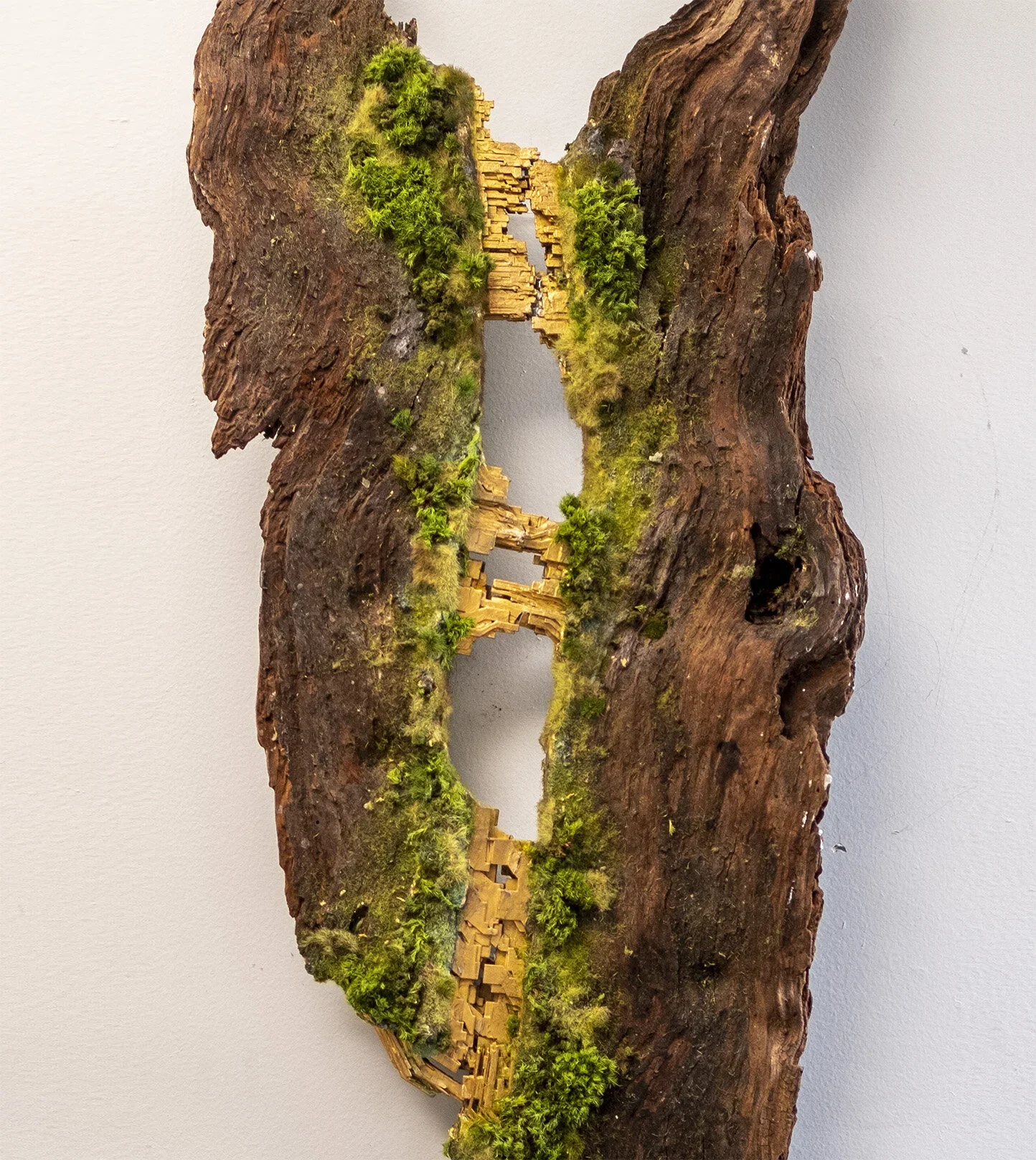 A piece of bark with moss and small wooden architectural models embedded in it.