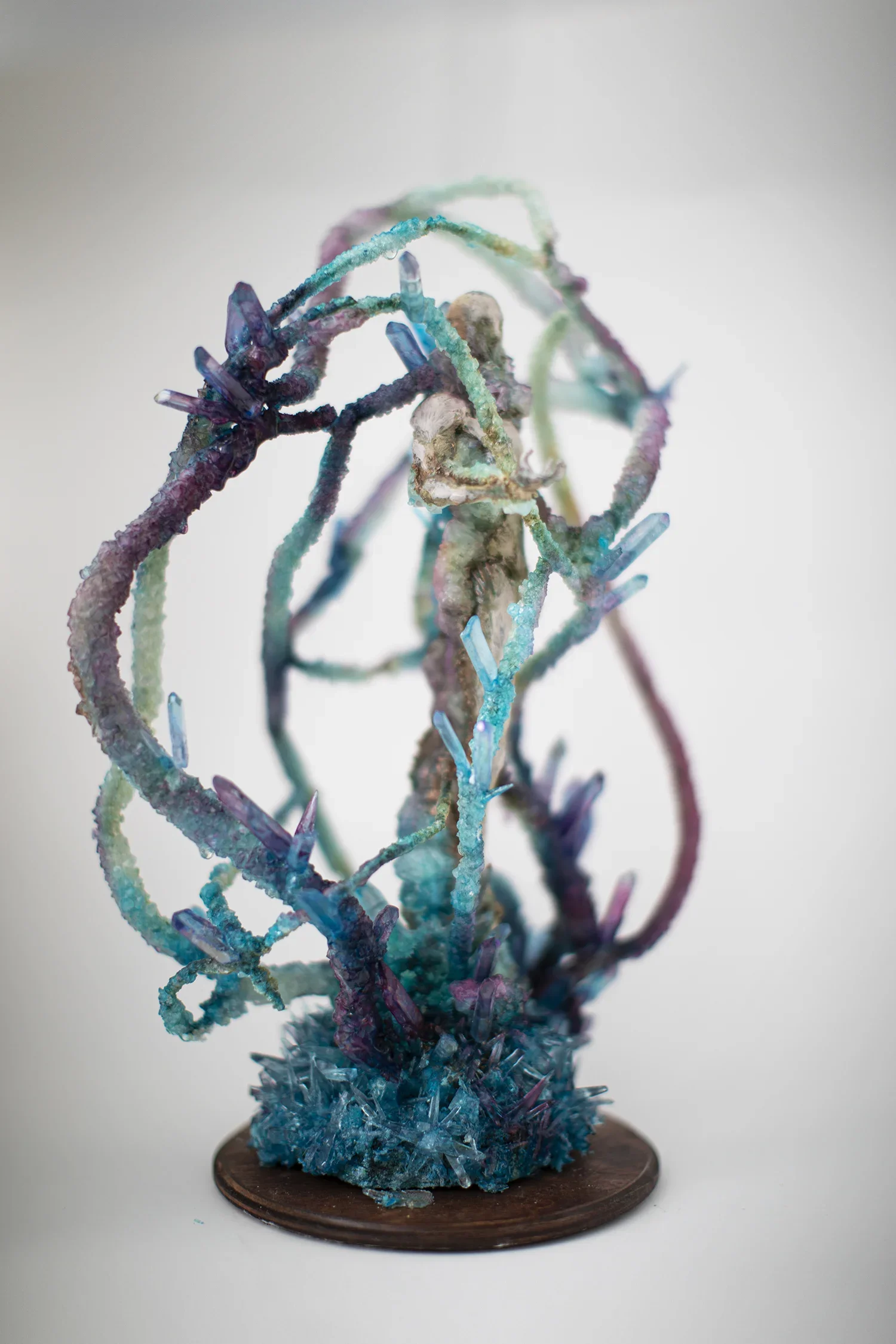 An abstract sculpture resembling a spiral or tree, made of colorful wire-like materials with crystal accents, mounted on a round wooden base.