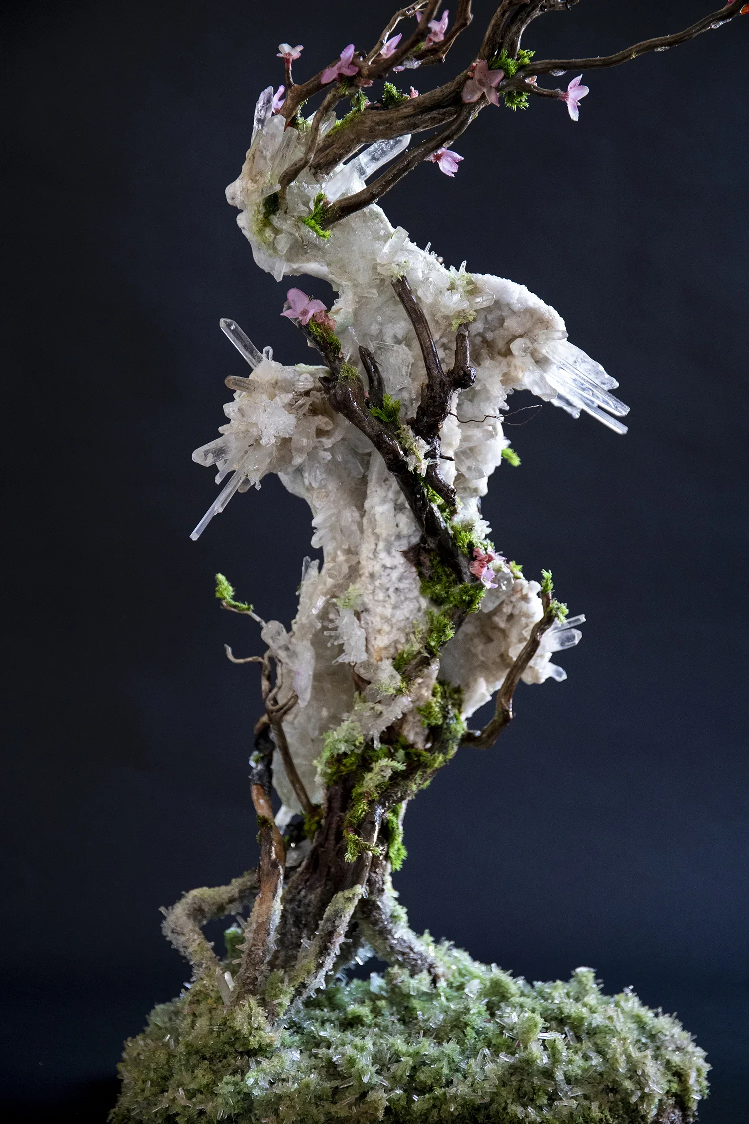 A sculpture of a horse made from natural materials such as branches, moss, crystals, and flowers set against a dark background.