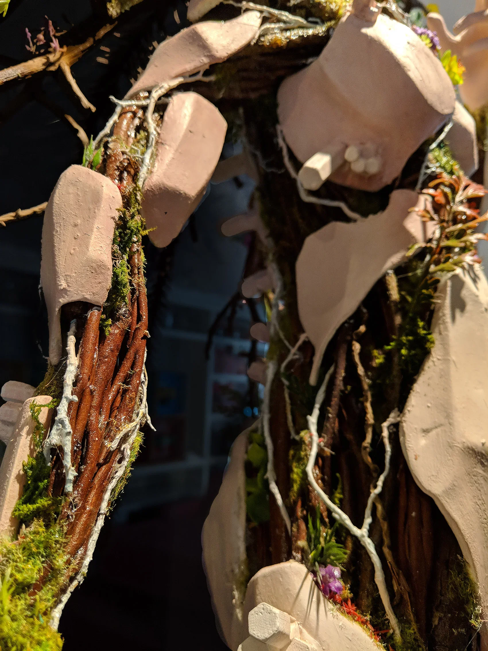 Close-up of a decorative outdoor feature made of white stones, intertwined with lit white string lights, moss, small plants, and twigs.