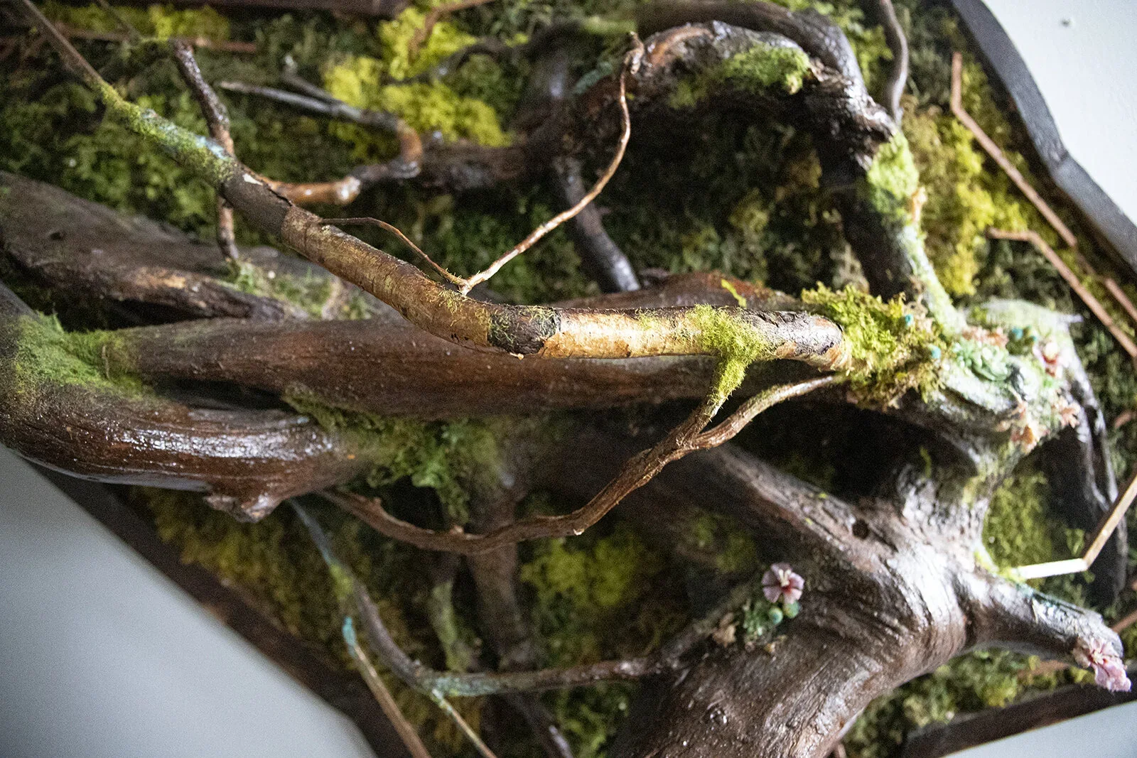 Close-up of moss-covered intertwined tree branches and roots with small colorful decorative flowers on moss and bark.