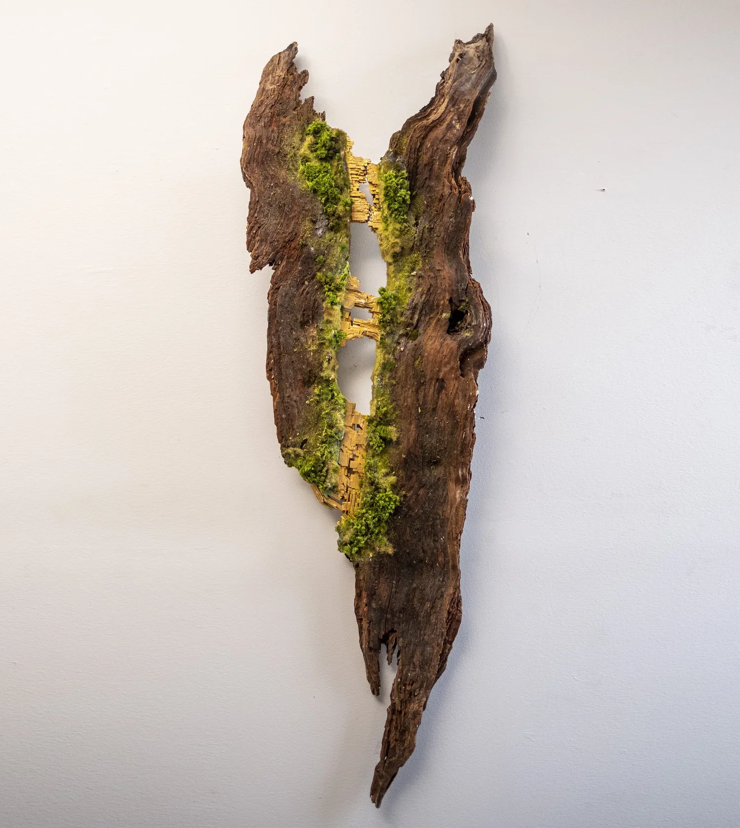 A piece of weathered wood with green moss, carved with small buildings, placed against a plain white background.