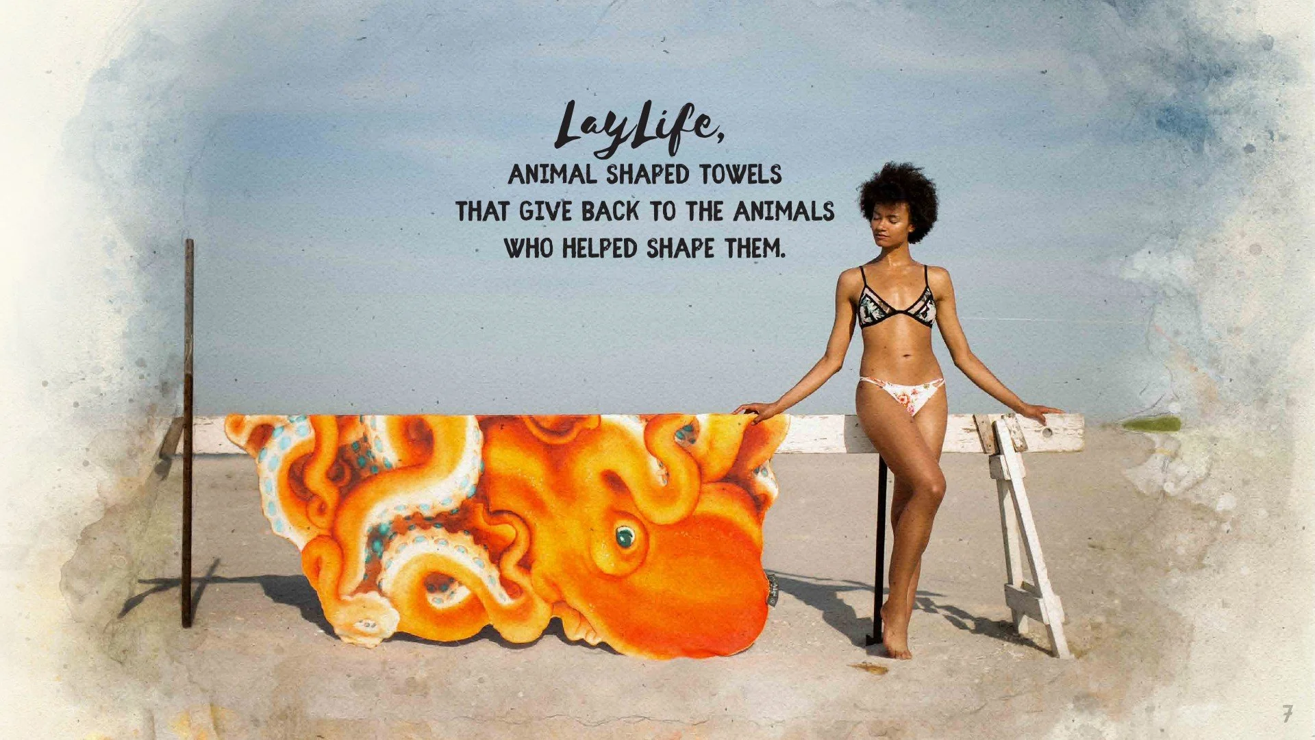 A woman in a bikini stands next to a bench on the beach, with a clouded sky in the background. A colorful octopus-shaped towel hangs over the bench, and a sign with the text "LayLife, animal-shaped towels that give back to the animals who helped shap