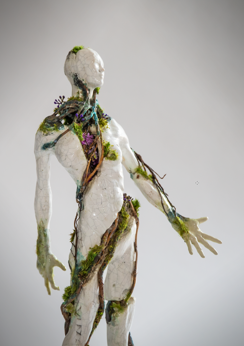 A sculpture of a human figure with a cracked white surface, intertwined with tree branches, moss, and purple flowers, resembling a merging of human and nature.