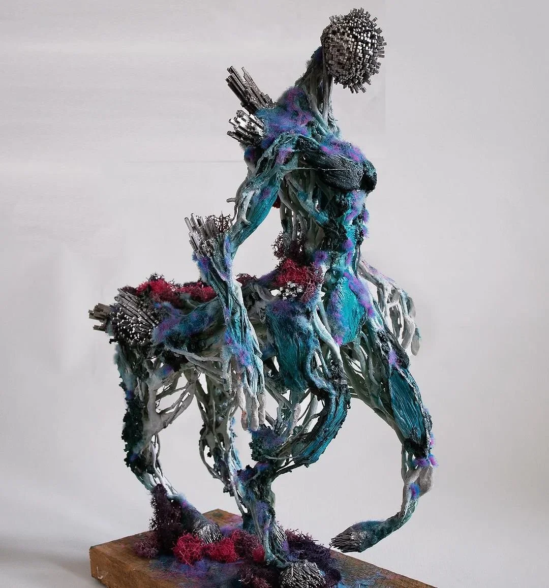 Mixed media sculpture of a humanoid figure with horse features, blending metallic, fabric, and organic materials.