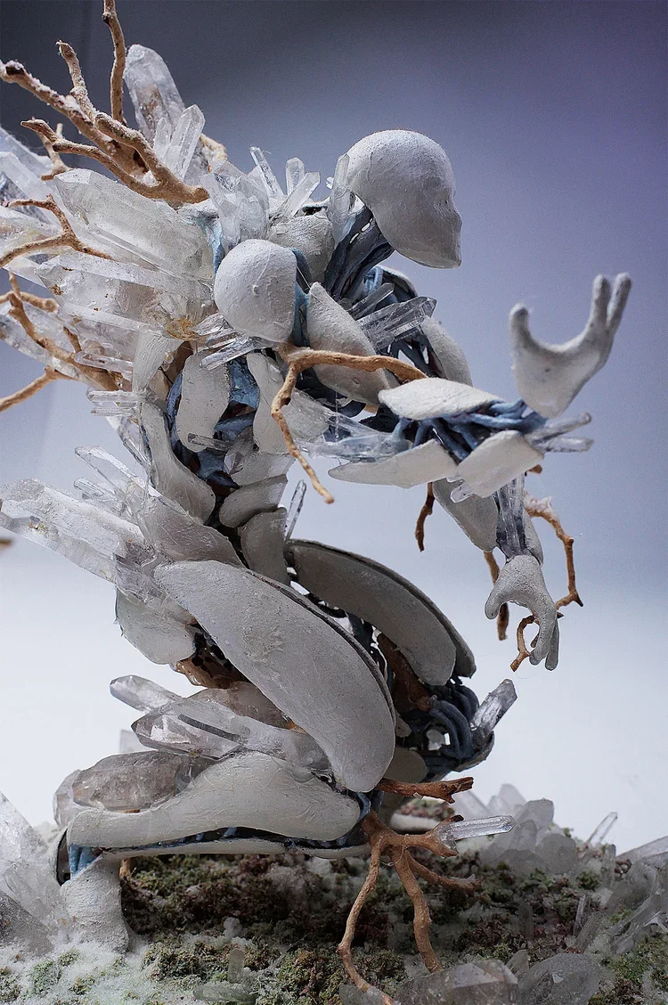 Sculpture of a person holding a baby, made with clay, plastic, and natural twigs.