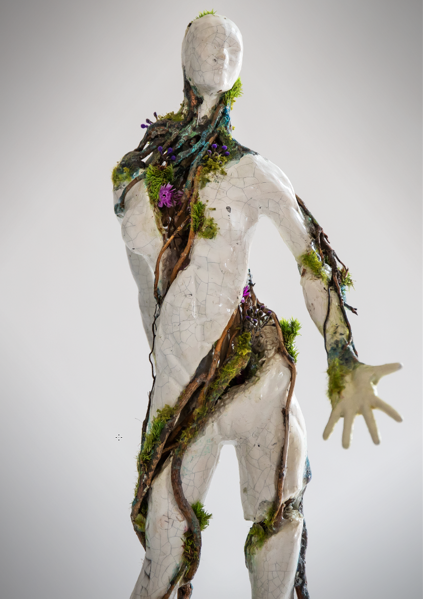 An art sculpture of a human figure with a cracked white surface, partially covered by intertwined roots, moss, and small purple flowers, with a blank face.