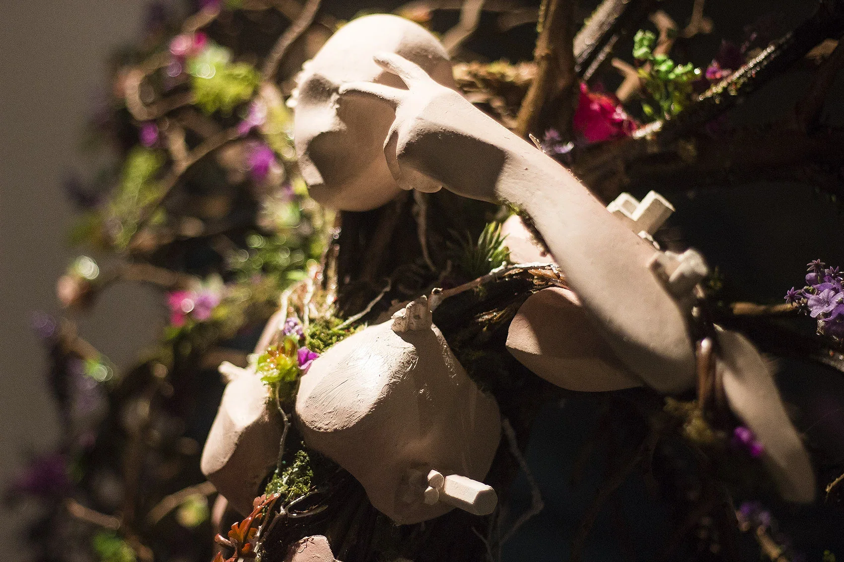 Close-up of a white sculpture of a person laying down surrounded by small purple, pink, and green plants and flowers.