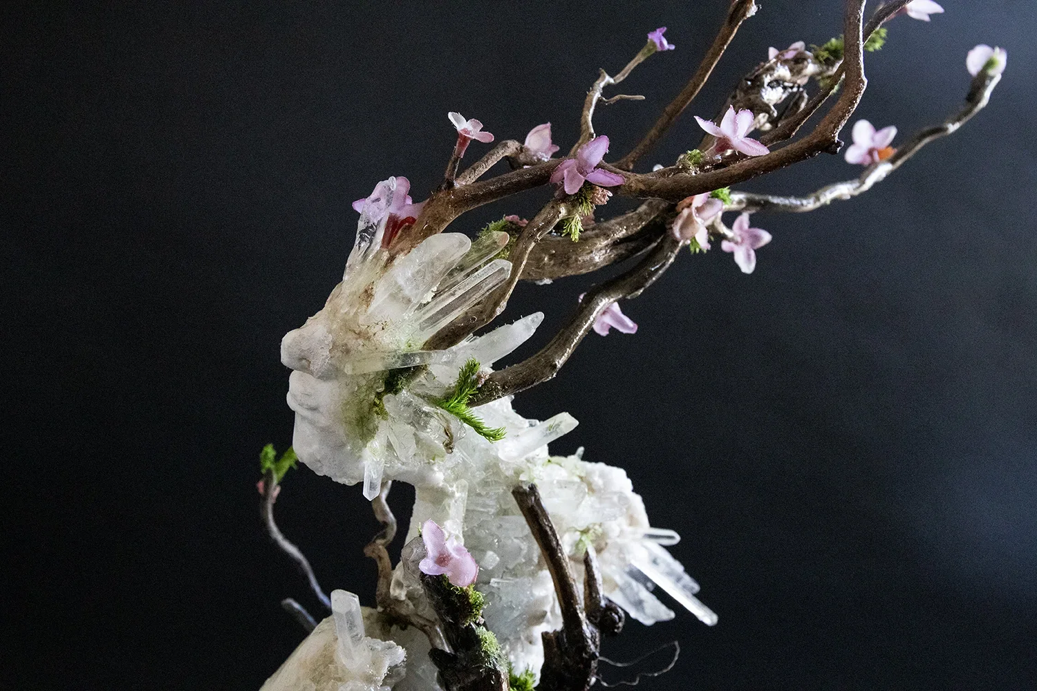 Artistic sculpture of pink flowers, tree branches, and crystal formations against a black background.