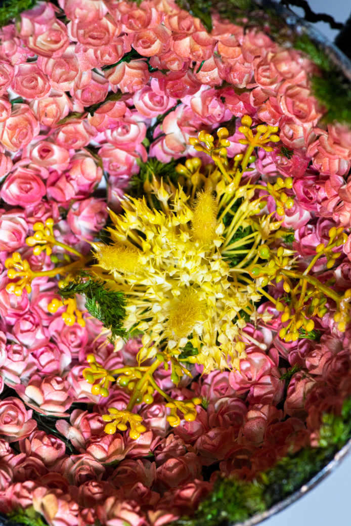 A floral arrangement with pink roses surrounding a central yellow and green floral centerpiece.