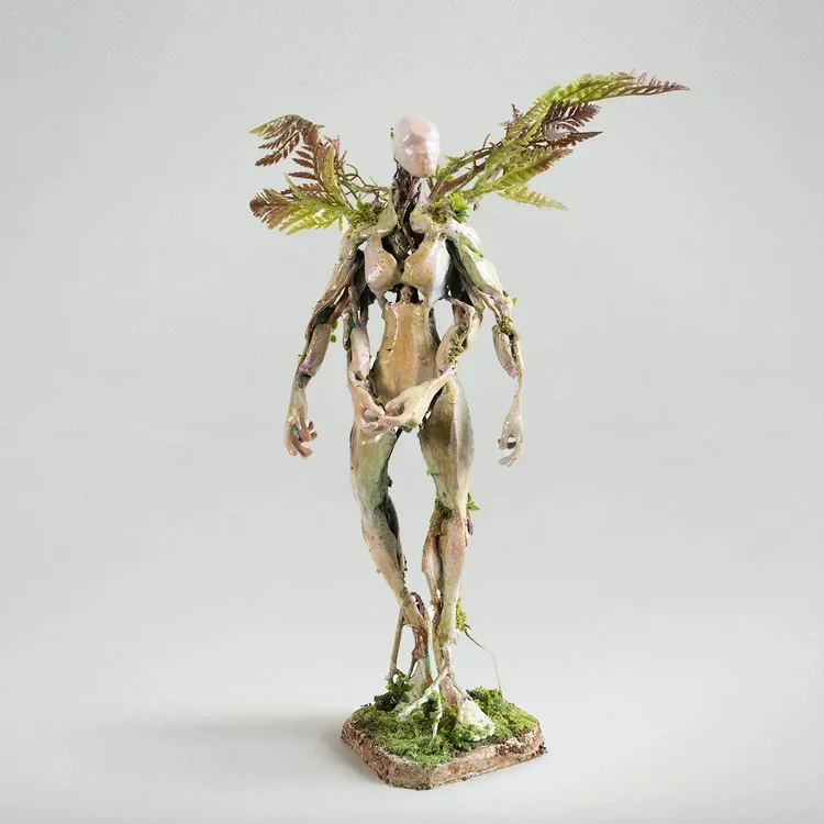 A sculpture of a humanoid figure with a nature-inspired design, featuring leaves and branches extending from its head and body, standing on a small base with moss.
