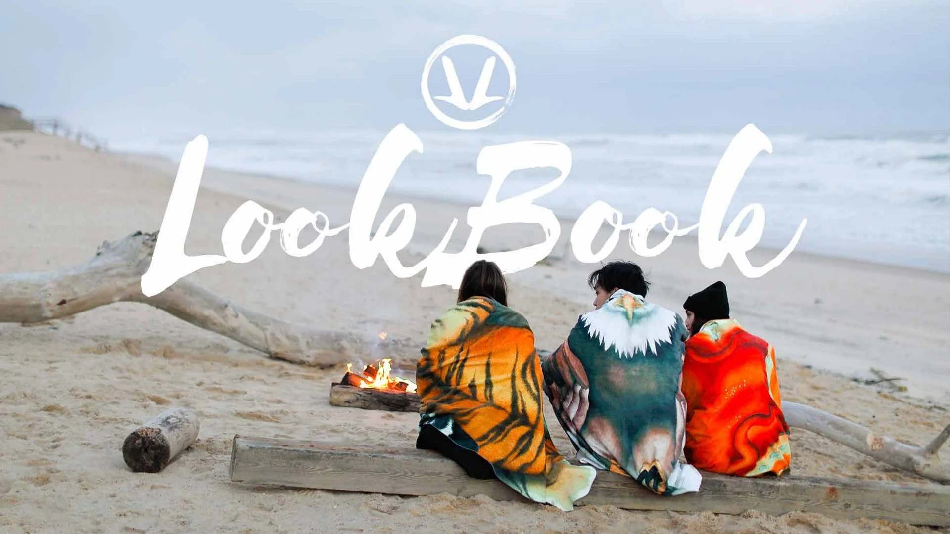 Three people sitting on the beach wrapped in colorful blankets, facing away from the camera, near a small fire with ocean waves in the background, with the words "Loki Book" overlaid.