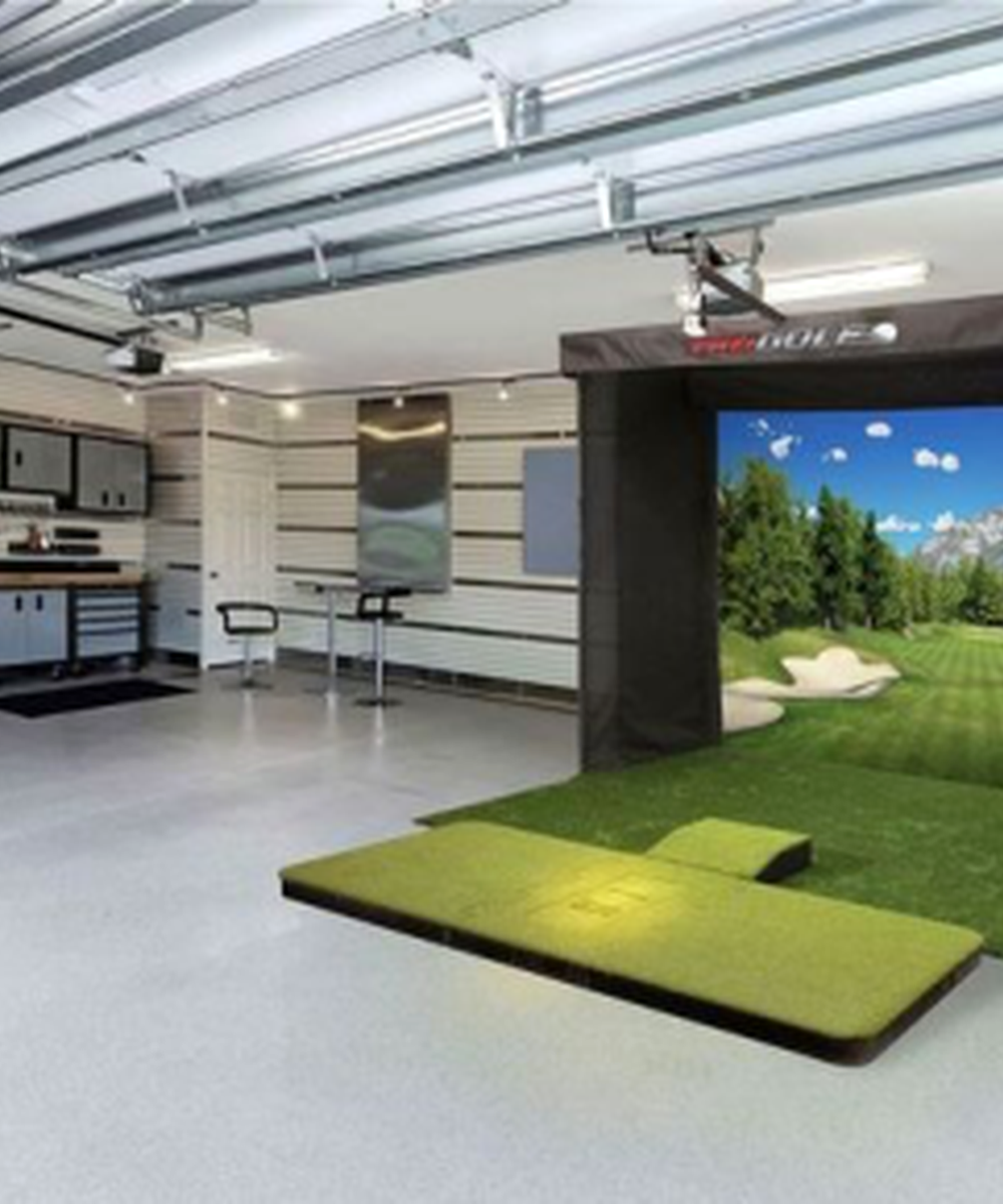 Indoor golf simulator room with a large screen showing a golf course, artificial turf, and cushioned seating.