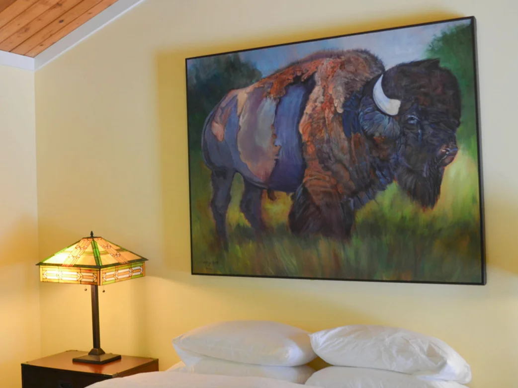 a painting of a buffalo sits above a bed in the Riverside building of Indian Creek Inn