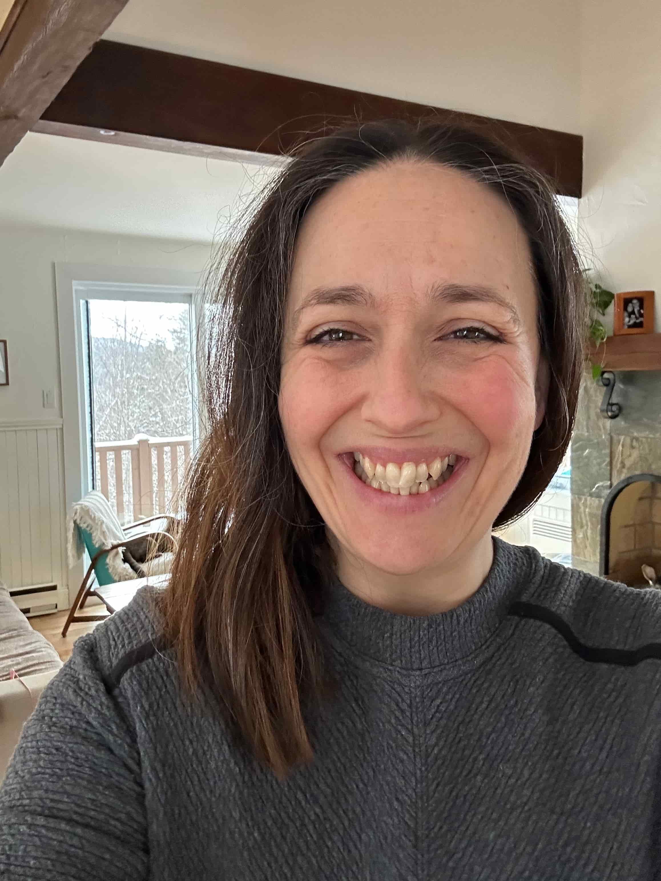 Woman with long brown hair hanging to one side wearing dark gray sweater smiling at camera