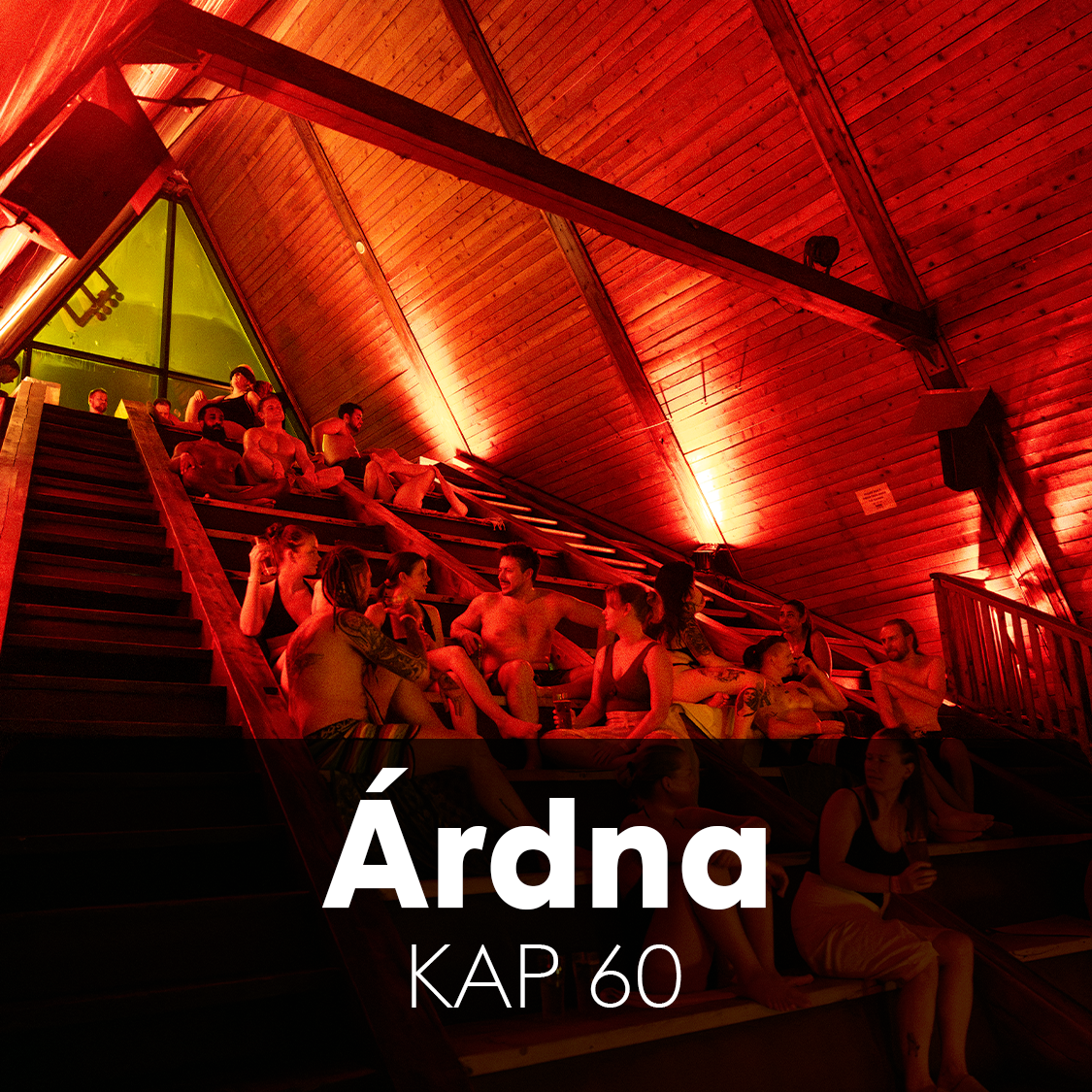 A group of people seated on tiered seating, watching a performance. The lighting is dim with red hues, and the audience appears engaged. The text overlay reads 'Árna KAP 60'.