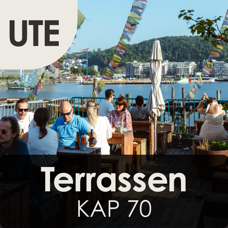 Outdoor terrace with people dining by the waterfront, colorful prayer flags, and a cityscape with hills in the background.