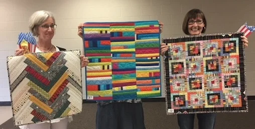Brenda Roach won 2017-18 Quilt Challenge, "Simply Stripes," with her "Stripe Tease" quilt. (Brenda is far right.) Katha Soens ' quilt is in the center. (Thanks, Laura, for holding it!) Wendy Hodina , holding her quilt, is far left.