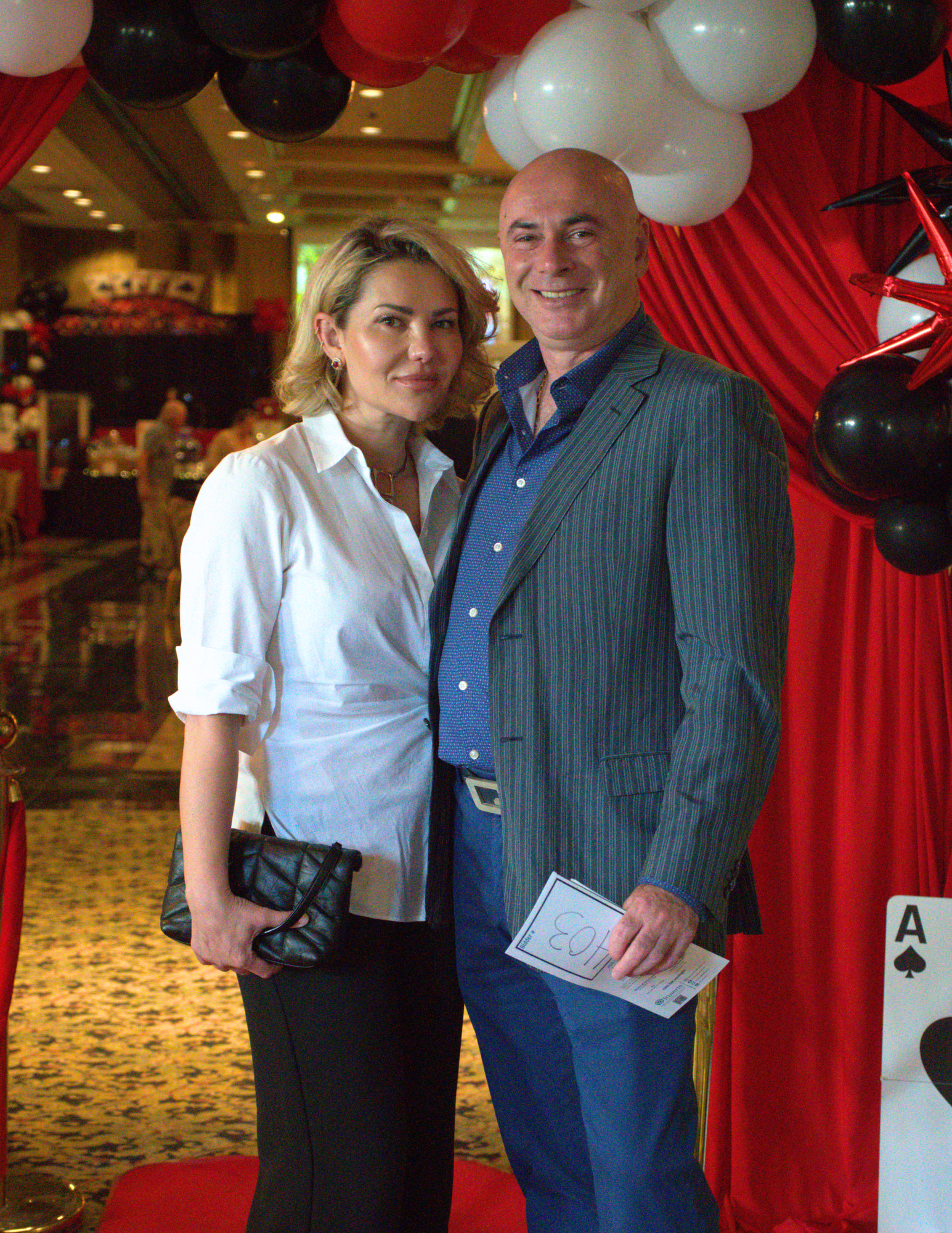a man and woman nicely dressed smiling at the camera in front of a red curtain.